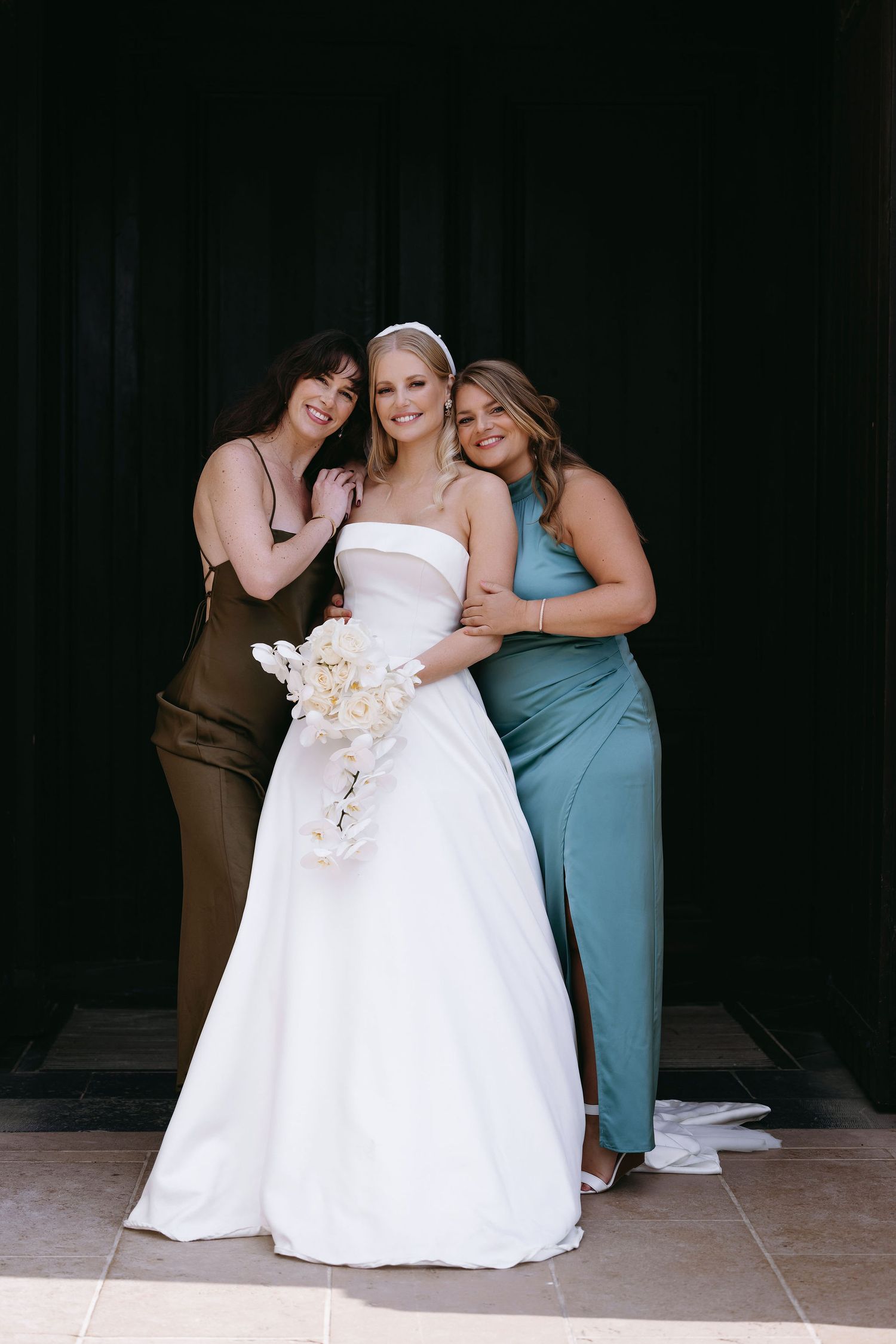 Two bridesmaids in blue dresses help adjust the bride's white wedding gown in a candid moment.