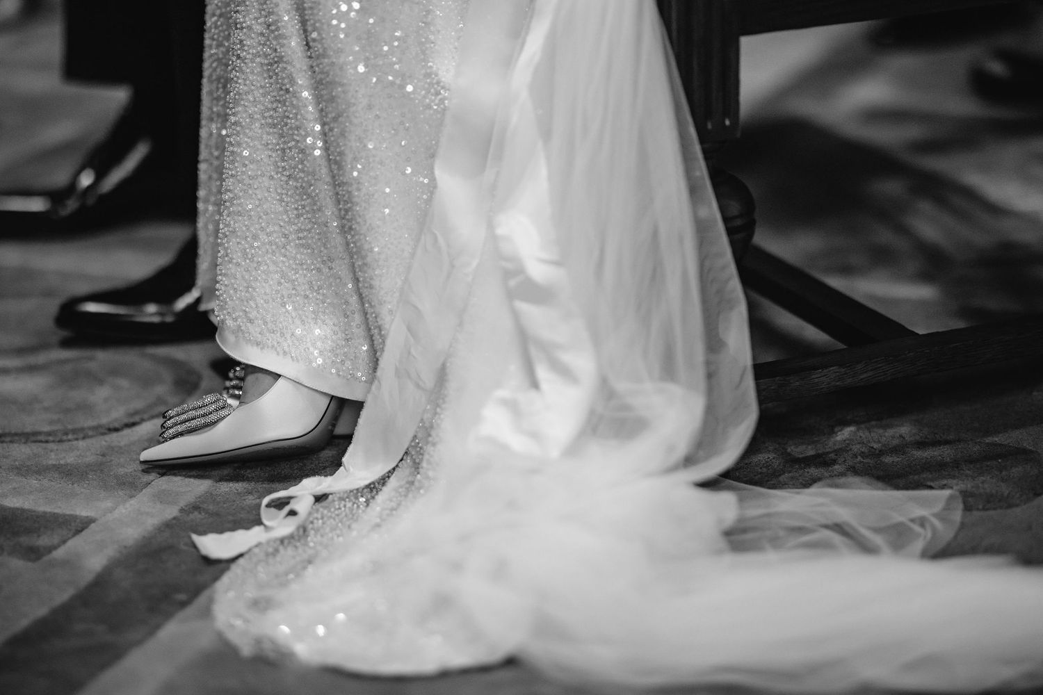 Close-up detail of sparkly wedding dress hem and formal shoes on a dance floor.