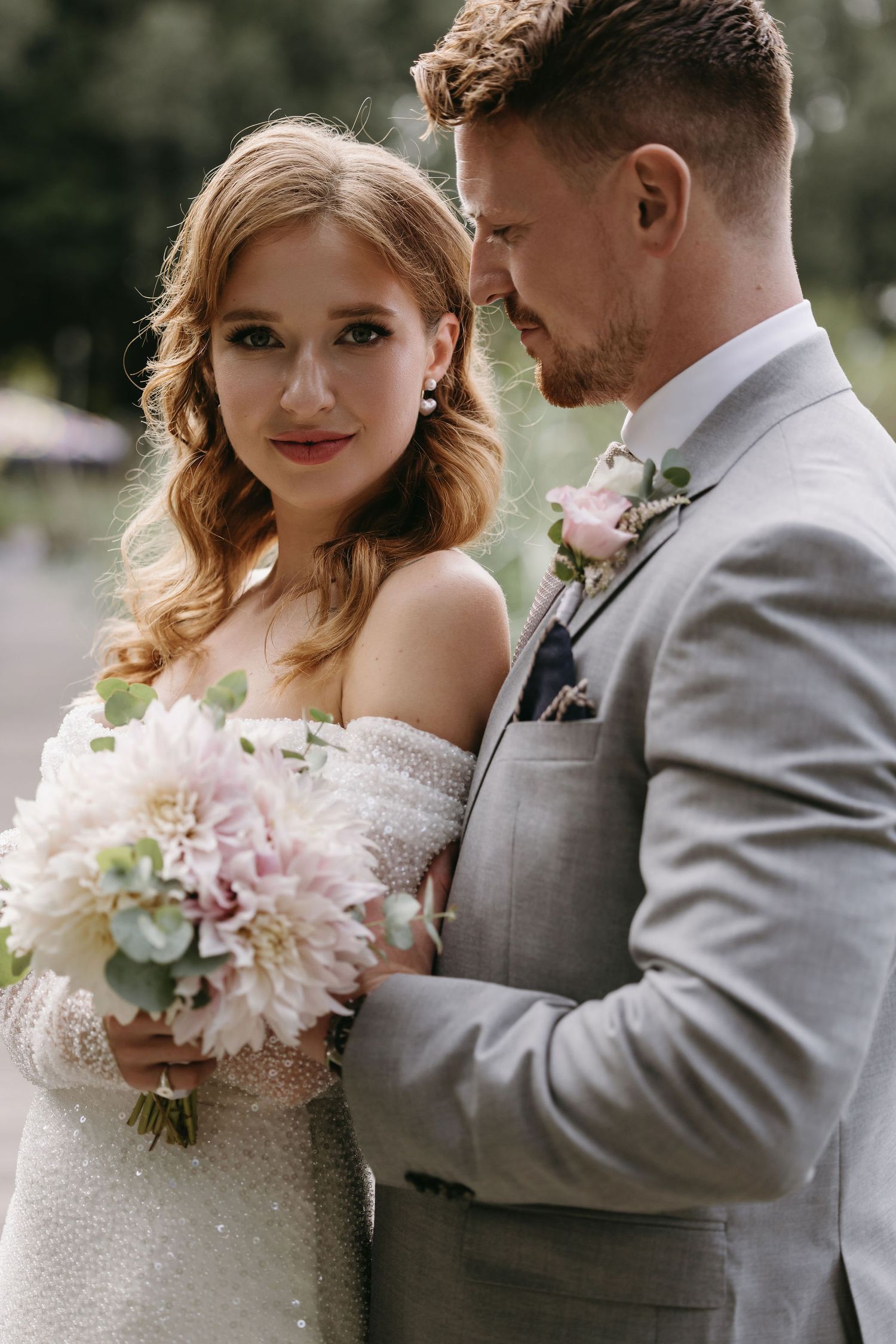 Couple poses with a pink and white wedding bouquet featuring dahlias and romantic details.