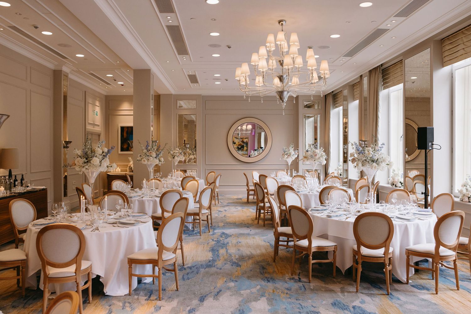 Elegant wedding reception ballroom with crystal chandeliers, white tablecloths, and cream-colored chairs in a luxurious setting.