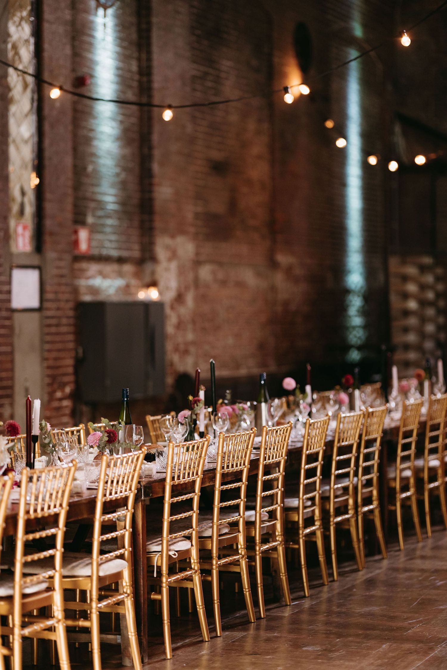 Long row of wooden chiavari chairs set up for wedding reception in rustic brick venue.