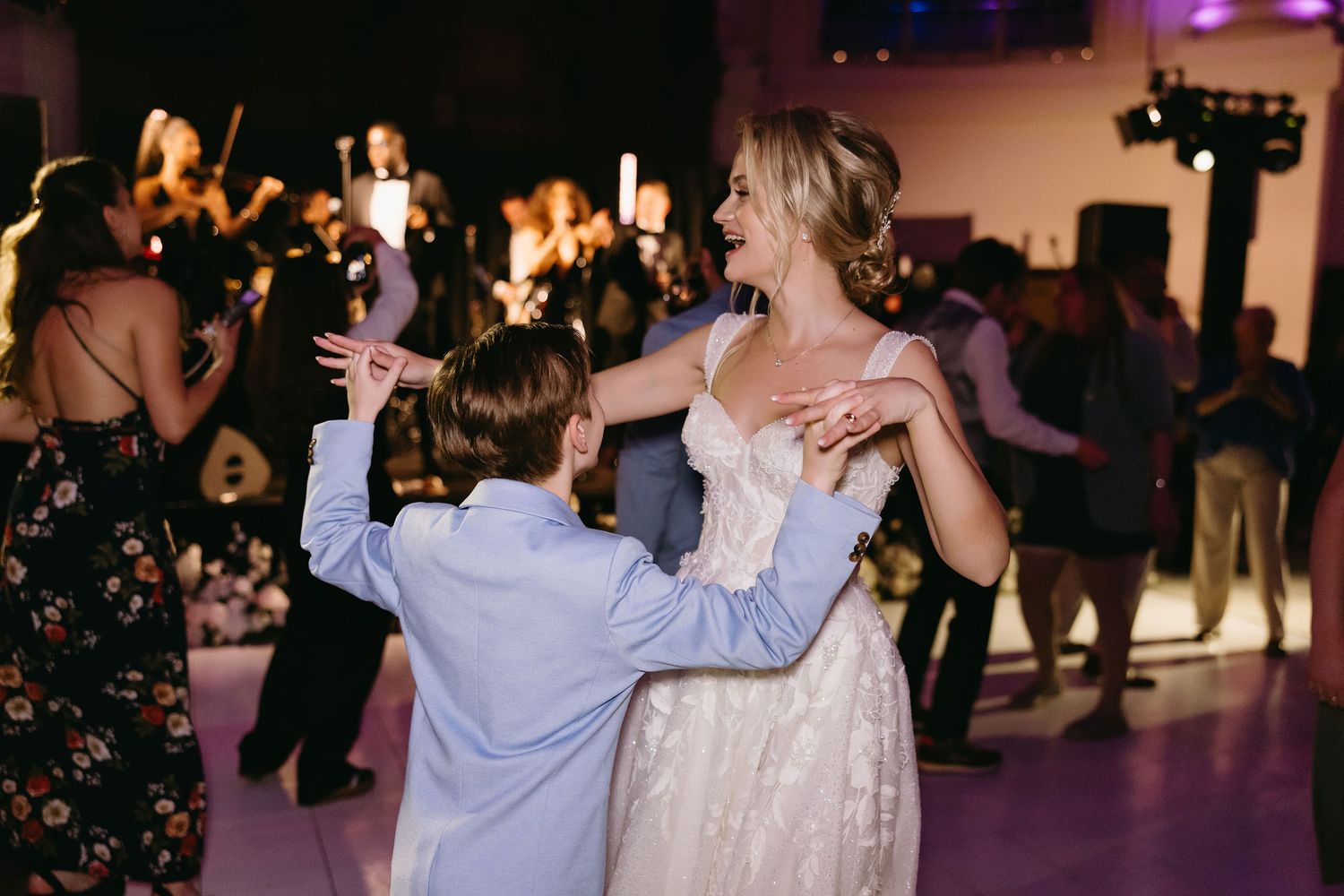 A young guest in a blue suit dances with a woman in a white dress at a wedding reception.