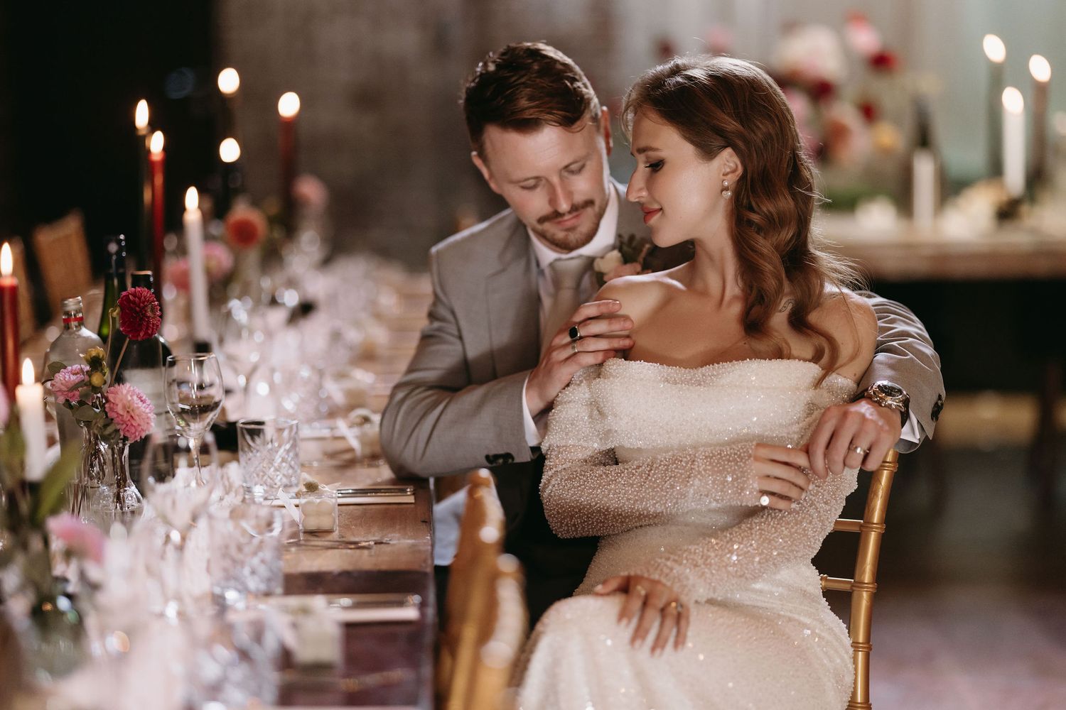 Wedding guests enjoying an intimate candlelit reception dinner with elegant table settings and warm lighting.