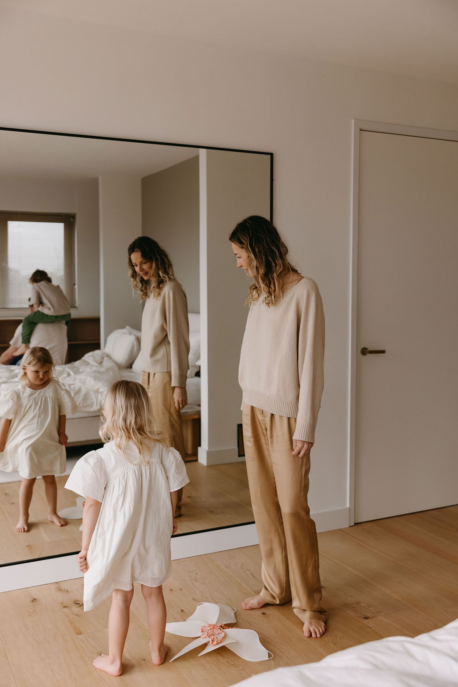 Mother and child standing by mirror in minimalist bedroom with wooden floors.