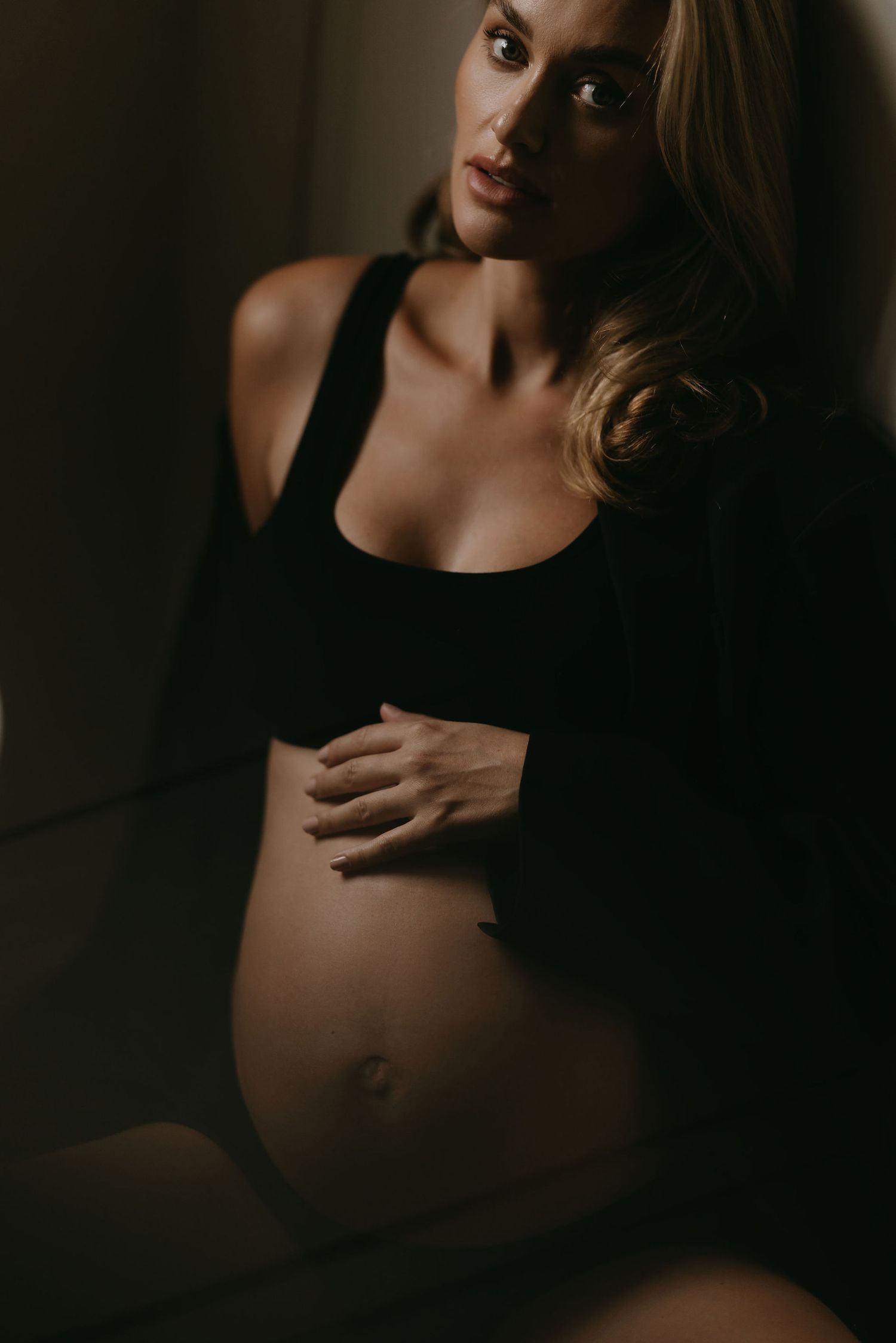 Dark and moody maternity portrait of pregnant woman in black top.