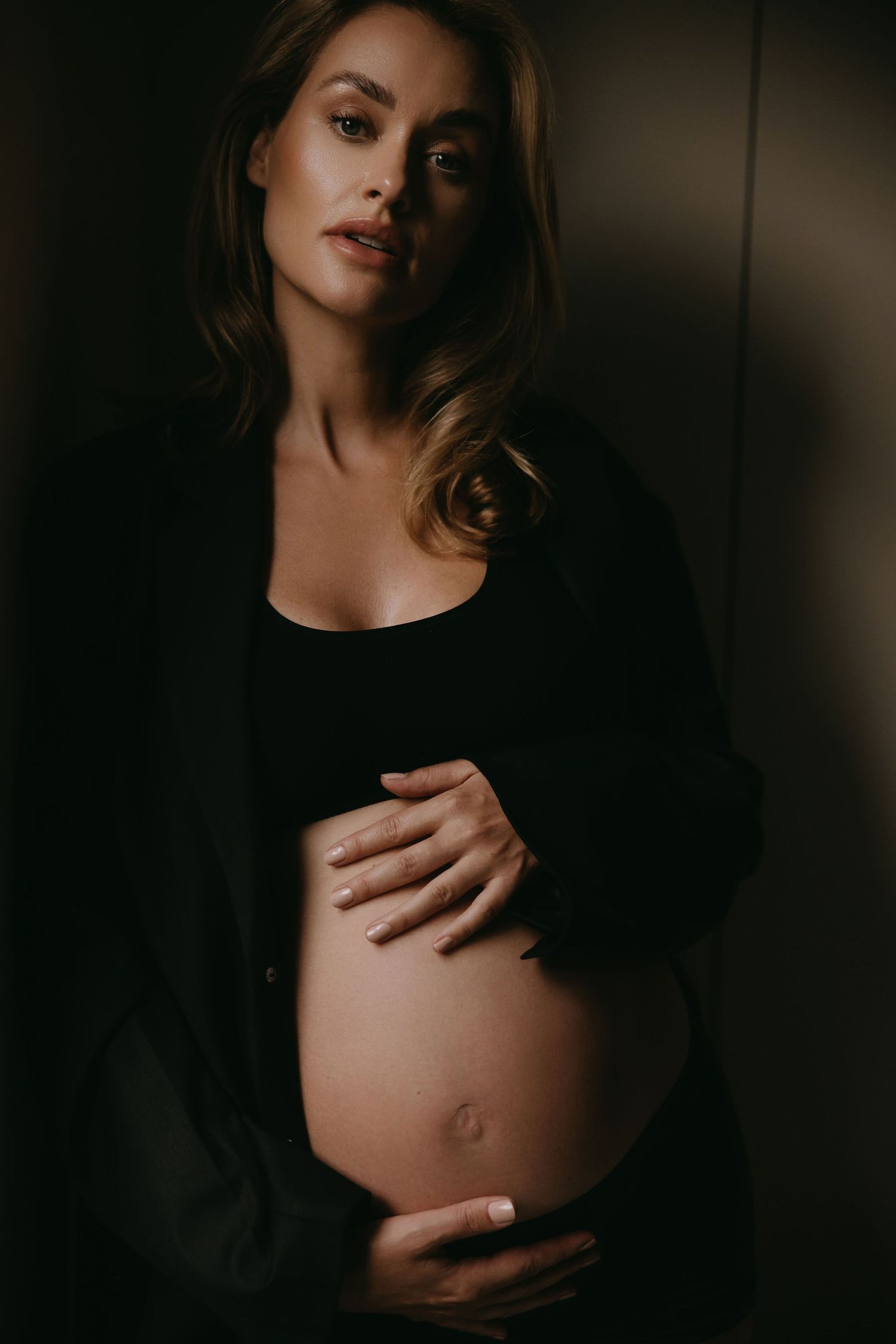 Dramatic maternity portrait in dark lighting showing pregnant silhouette.