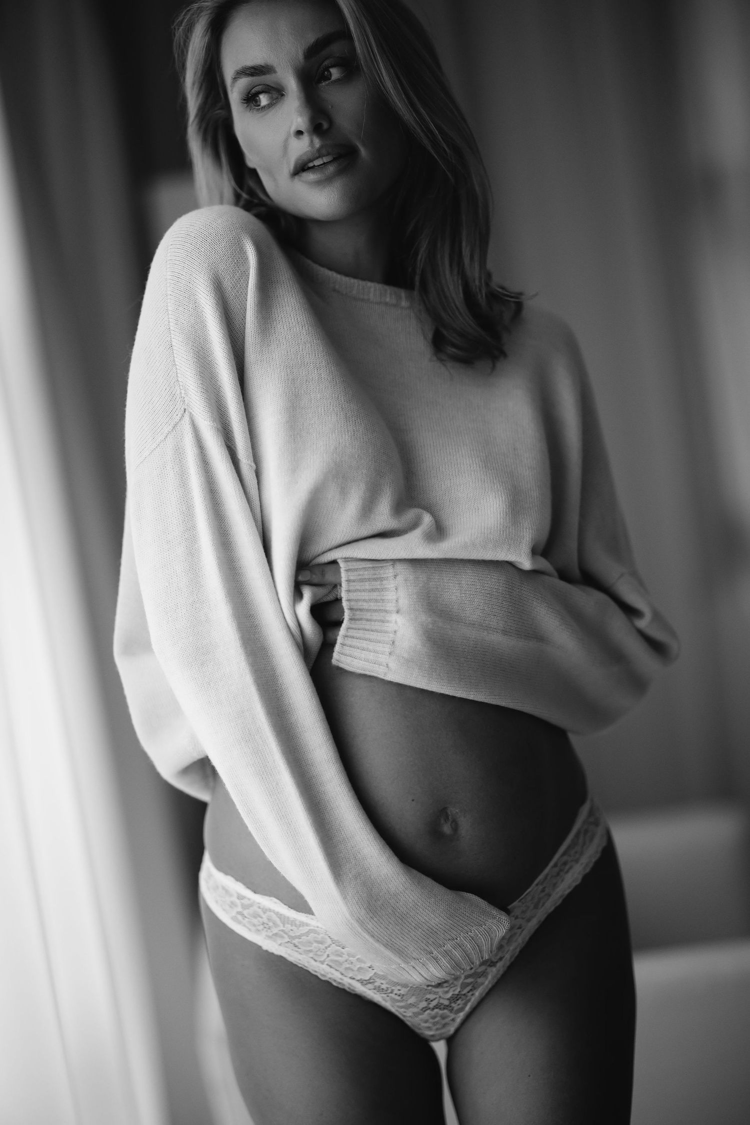 Black and white portrait in cozy sweater against window light.