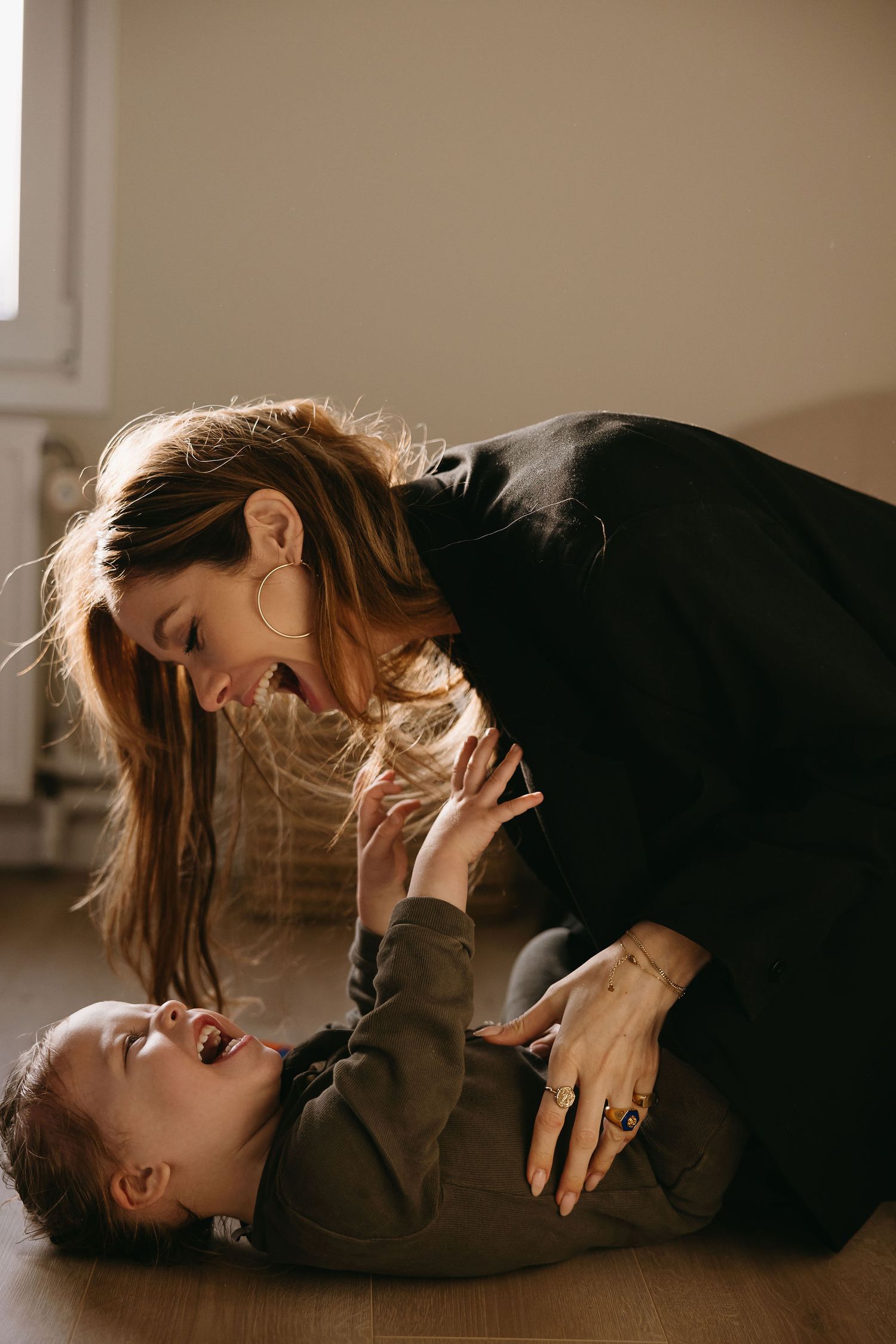 Mother and child share intimate playful moment on wooden floor.