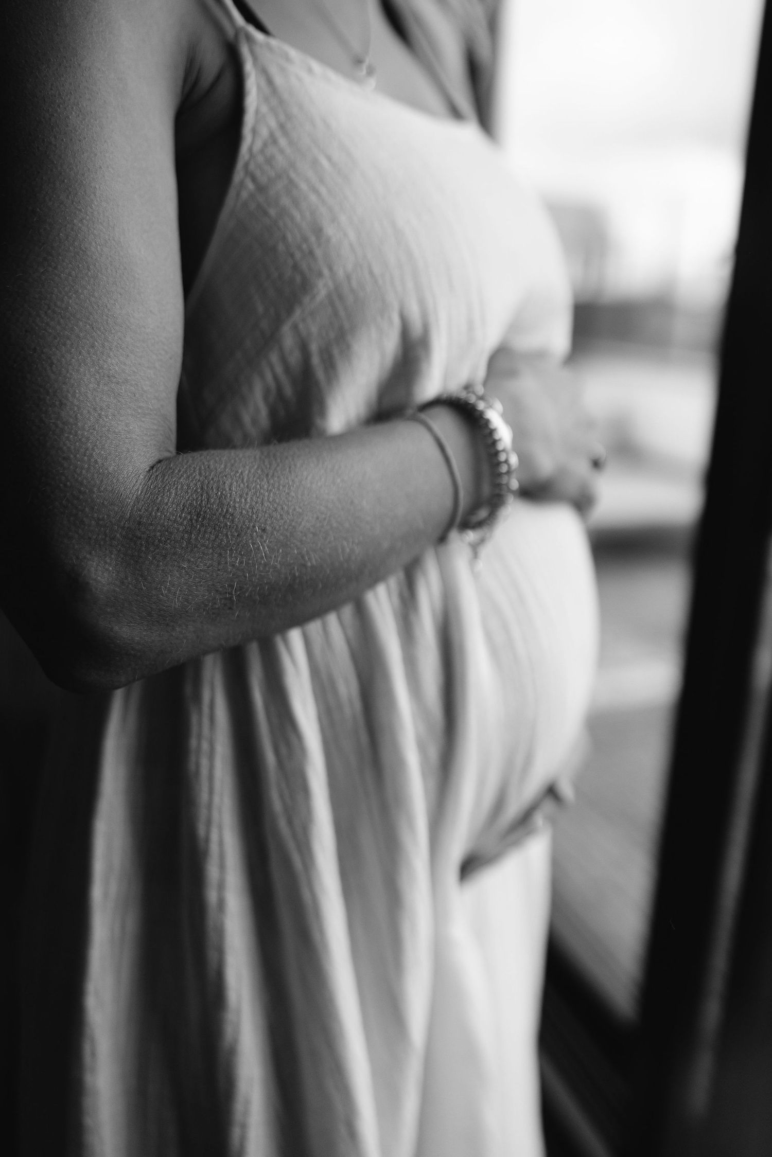 Close-up black and white photo of a pregnant belly in a flowing white dress.