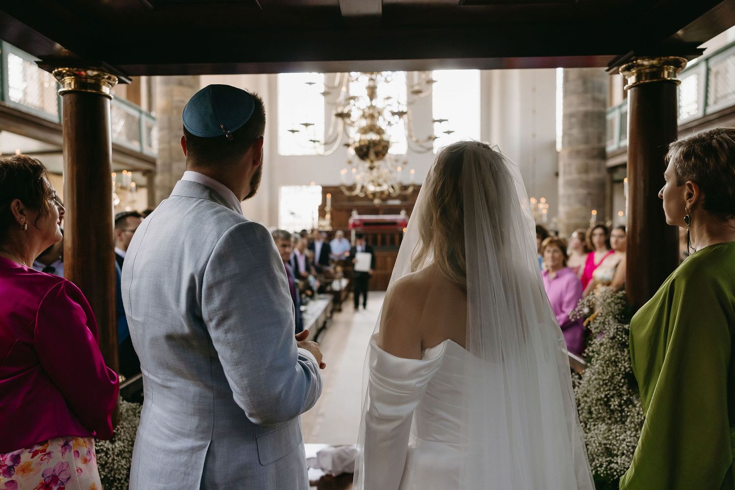 Wedding processional in a traditional church with ornate lighting and natural sunlight streaming through windows.