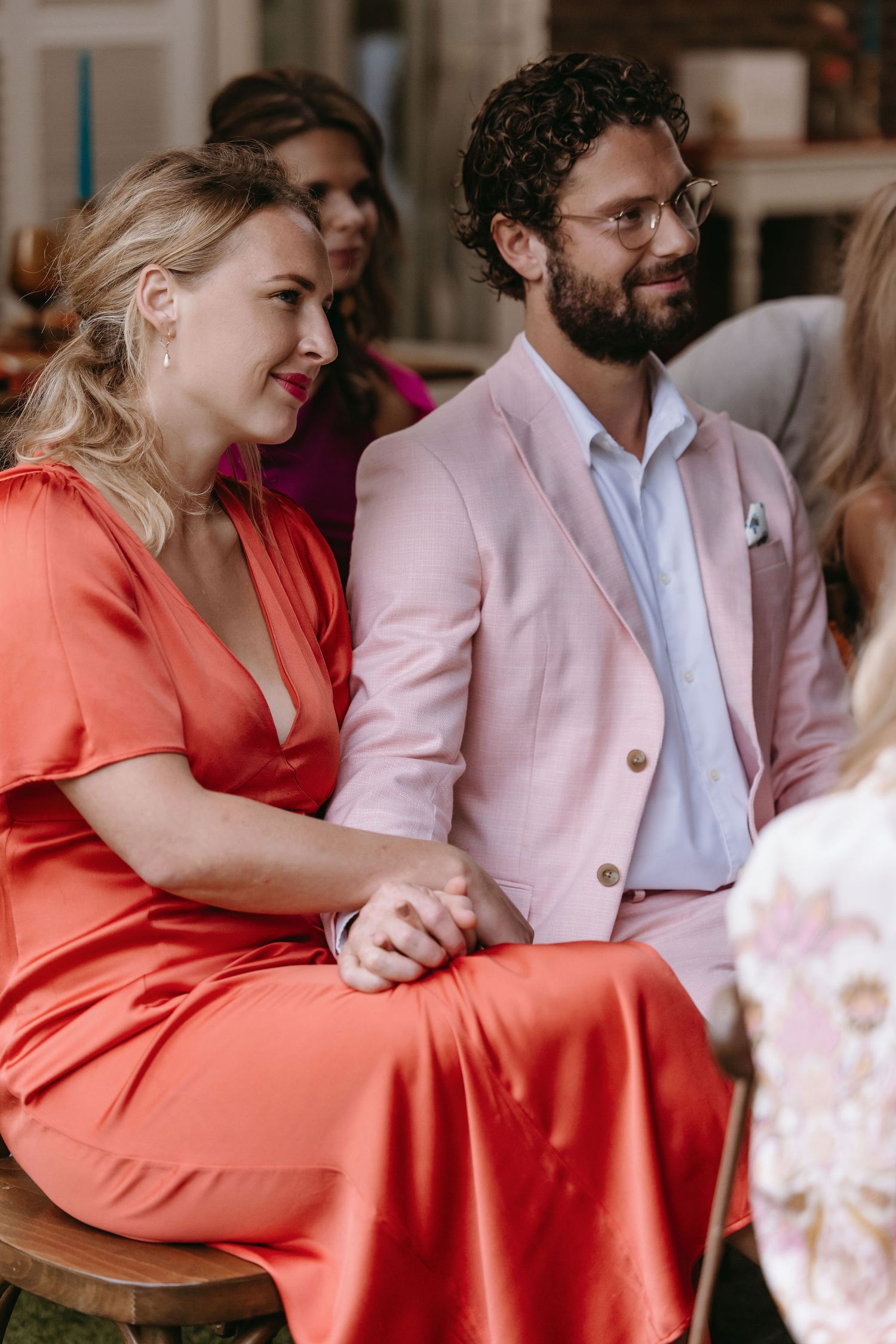 Wedding guests in coral and pink attire sharing joyful moments at reception.