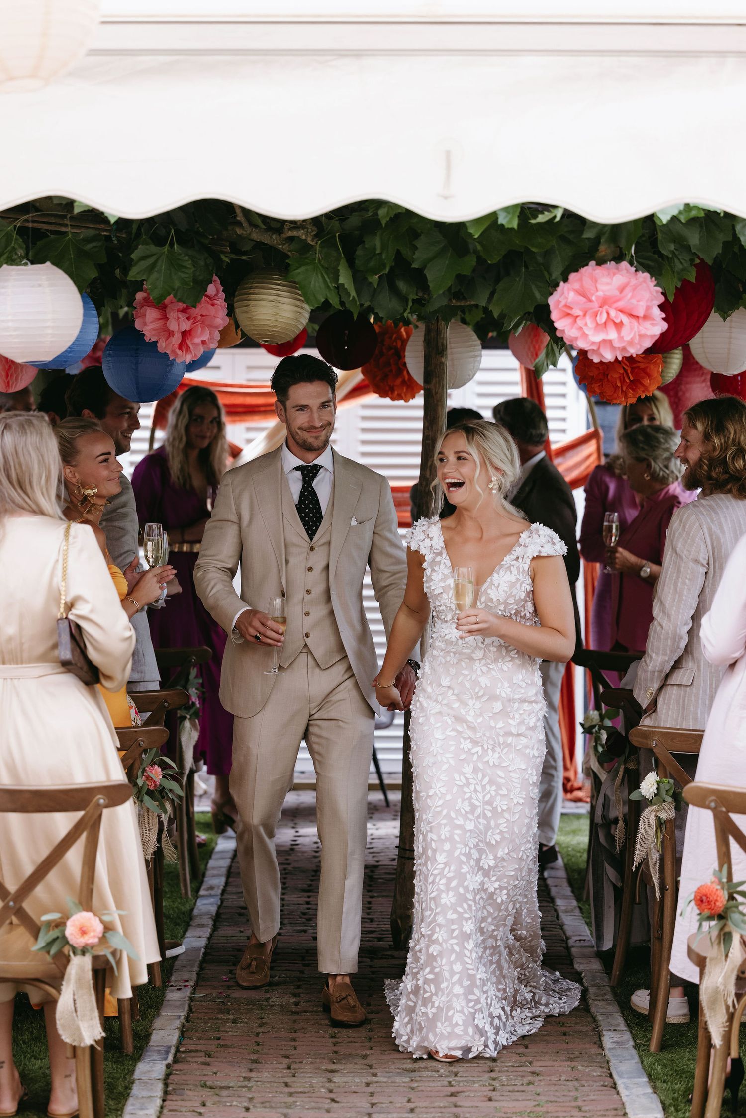 Wedding celebration under a tent decorated with pink lanterns and greenery.