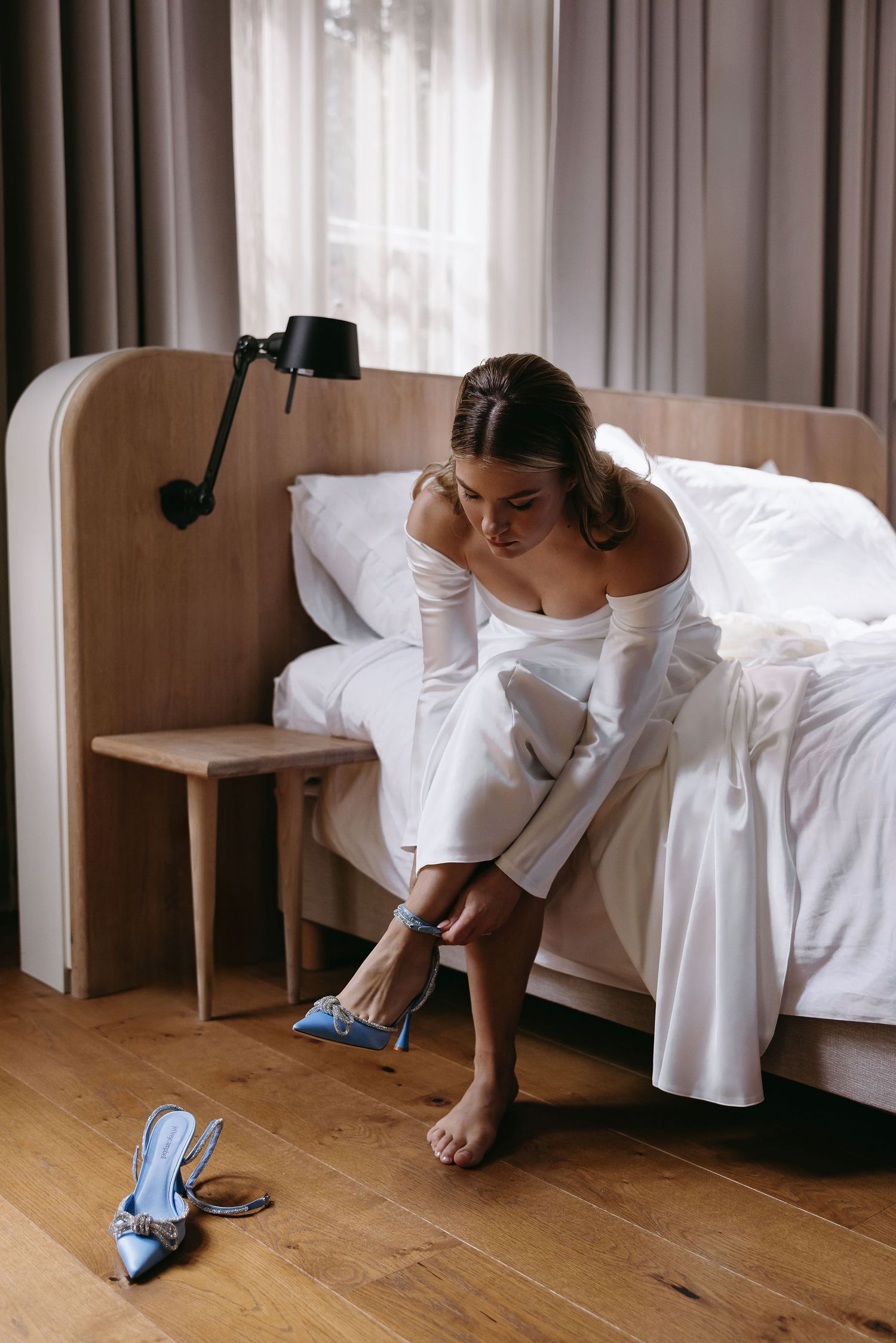 Sequence showing person in white dress putting on blue shoes on wooden floor.