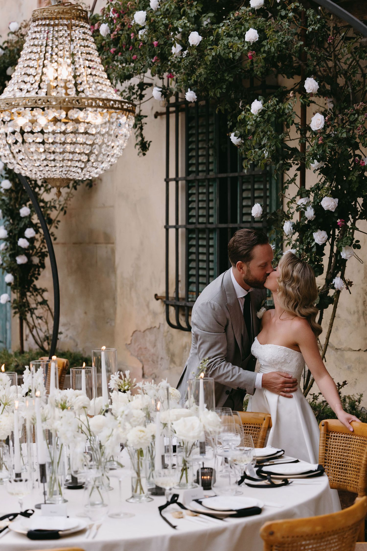Elegant outdoor wedding reception setup with crystal chandeliers, white table settings, and romantic couple moments.
