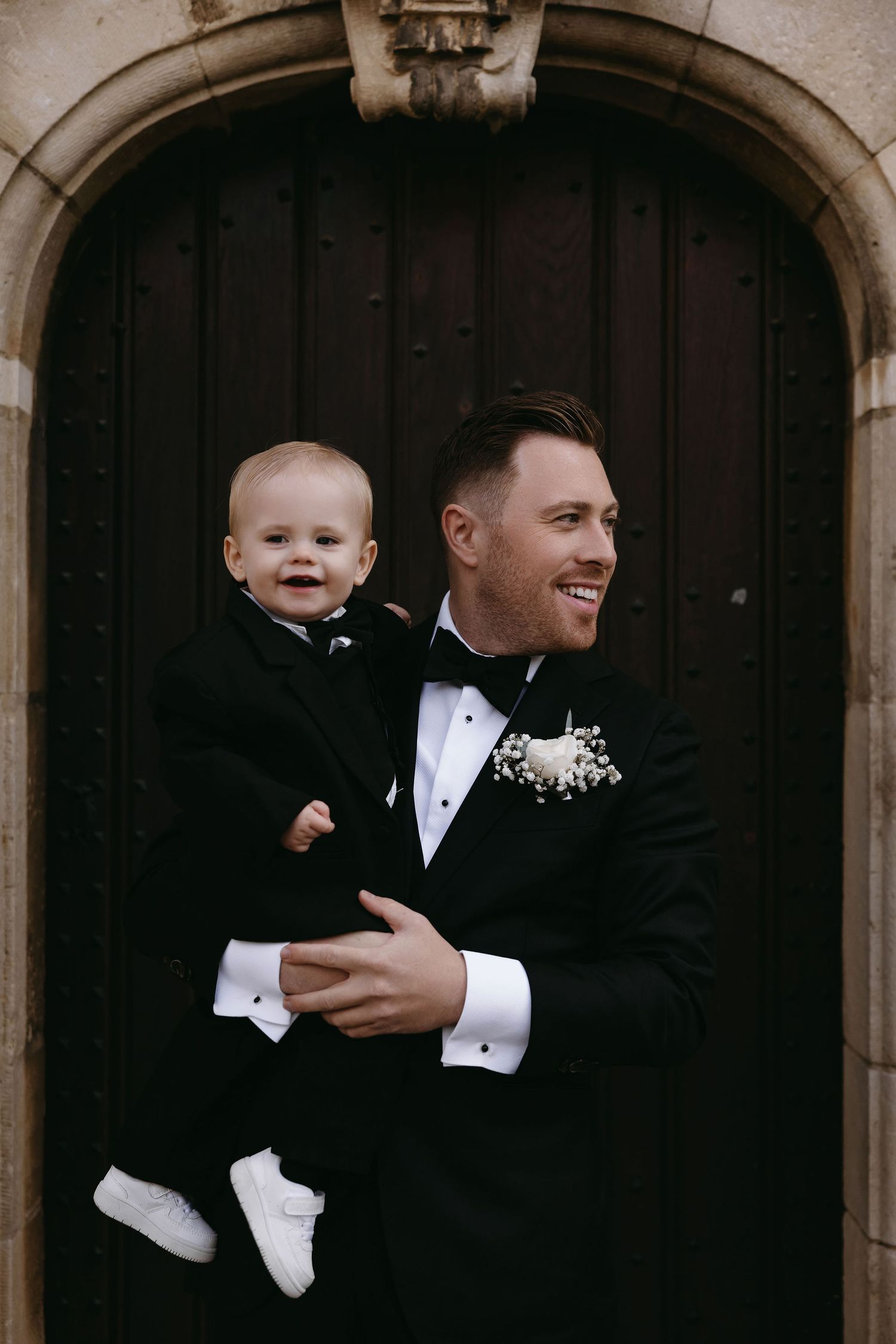 Formal portrait under stone archways with person holding baby in matching formal attire.