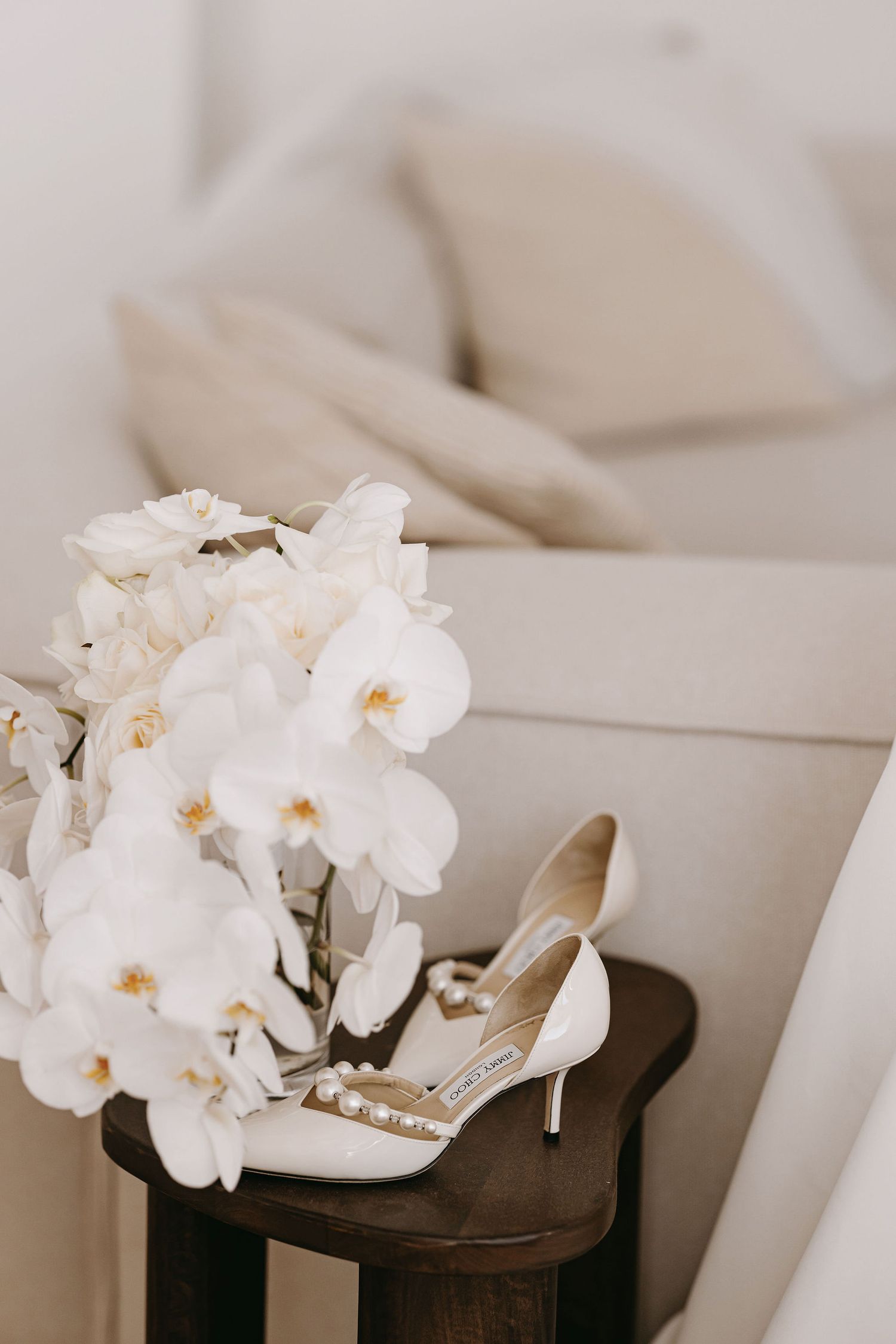 White orchid flowers and bridal shoes arranged artistically on light neutral fabric.