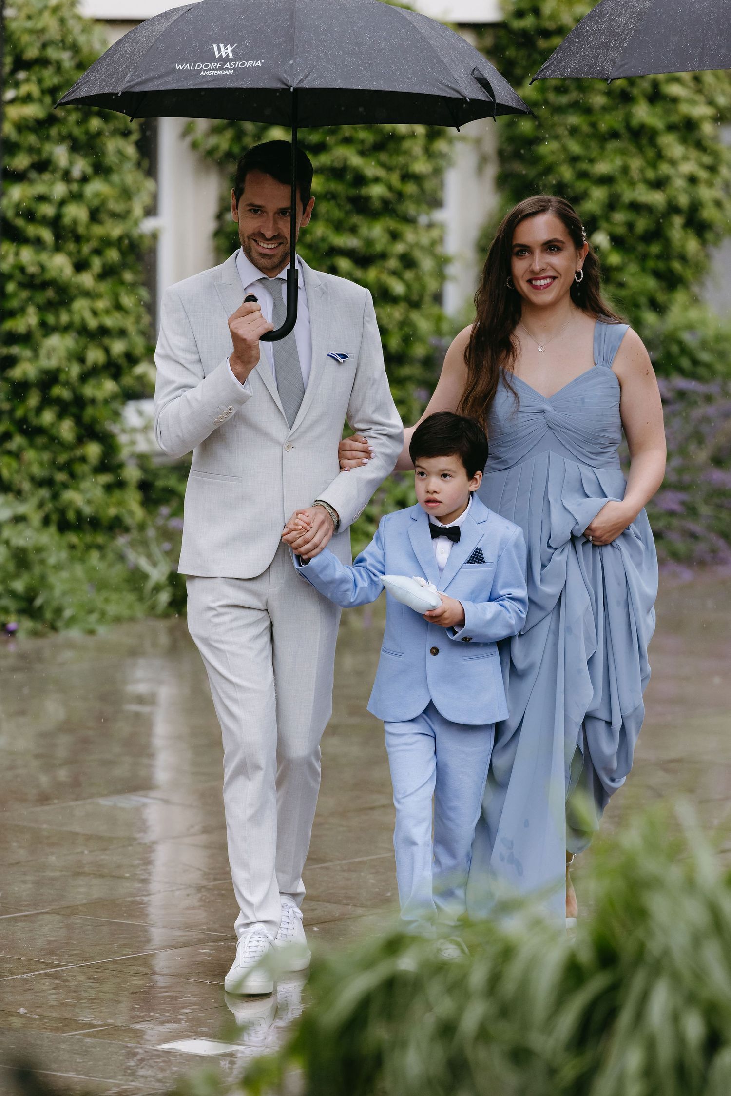 Family walking in rain with umbrellas, featuring matching light blue and white formal attire.