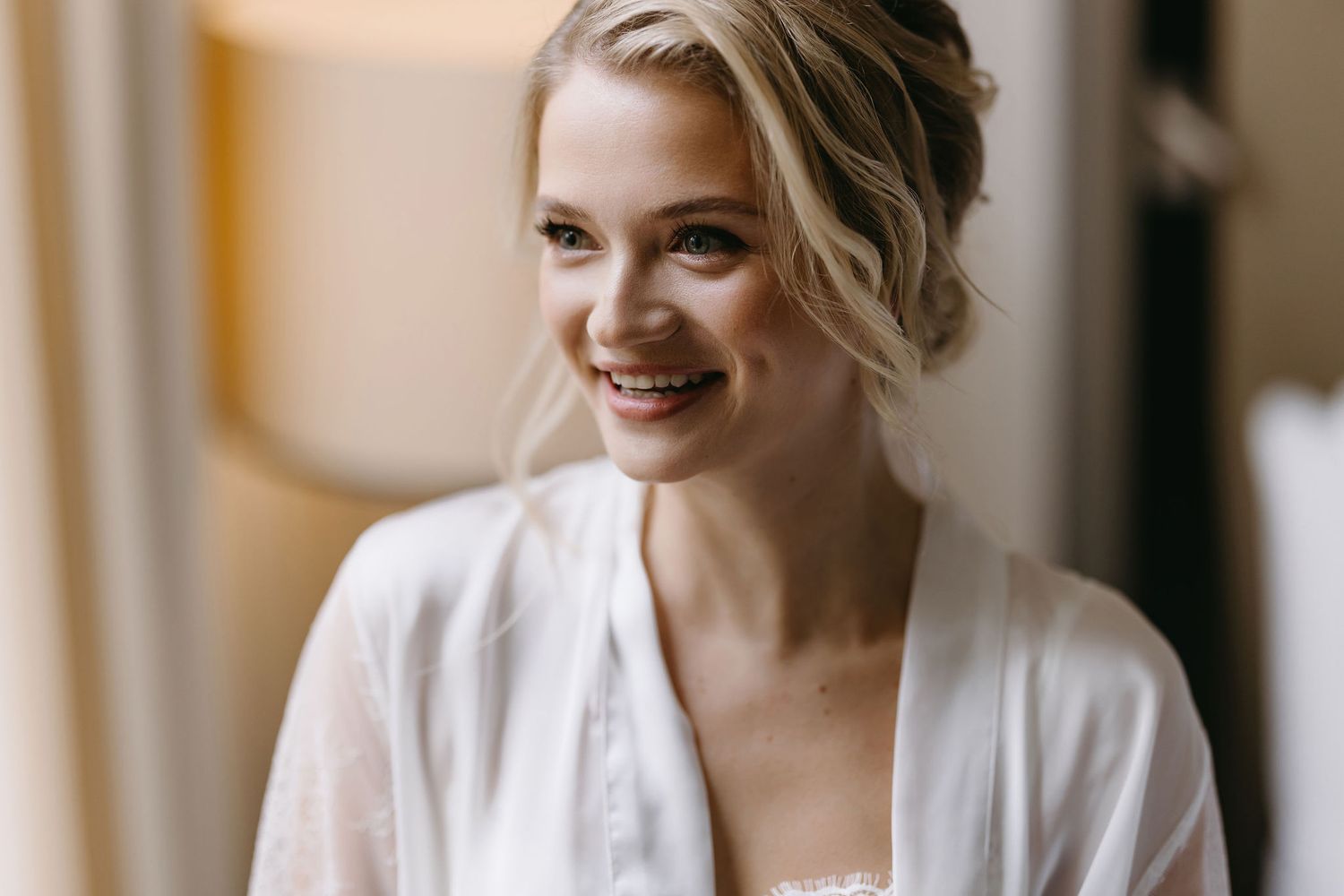A romantic wedding morning preparation scene in a bright sunlit room with soft lighting and white decor.