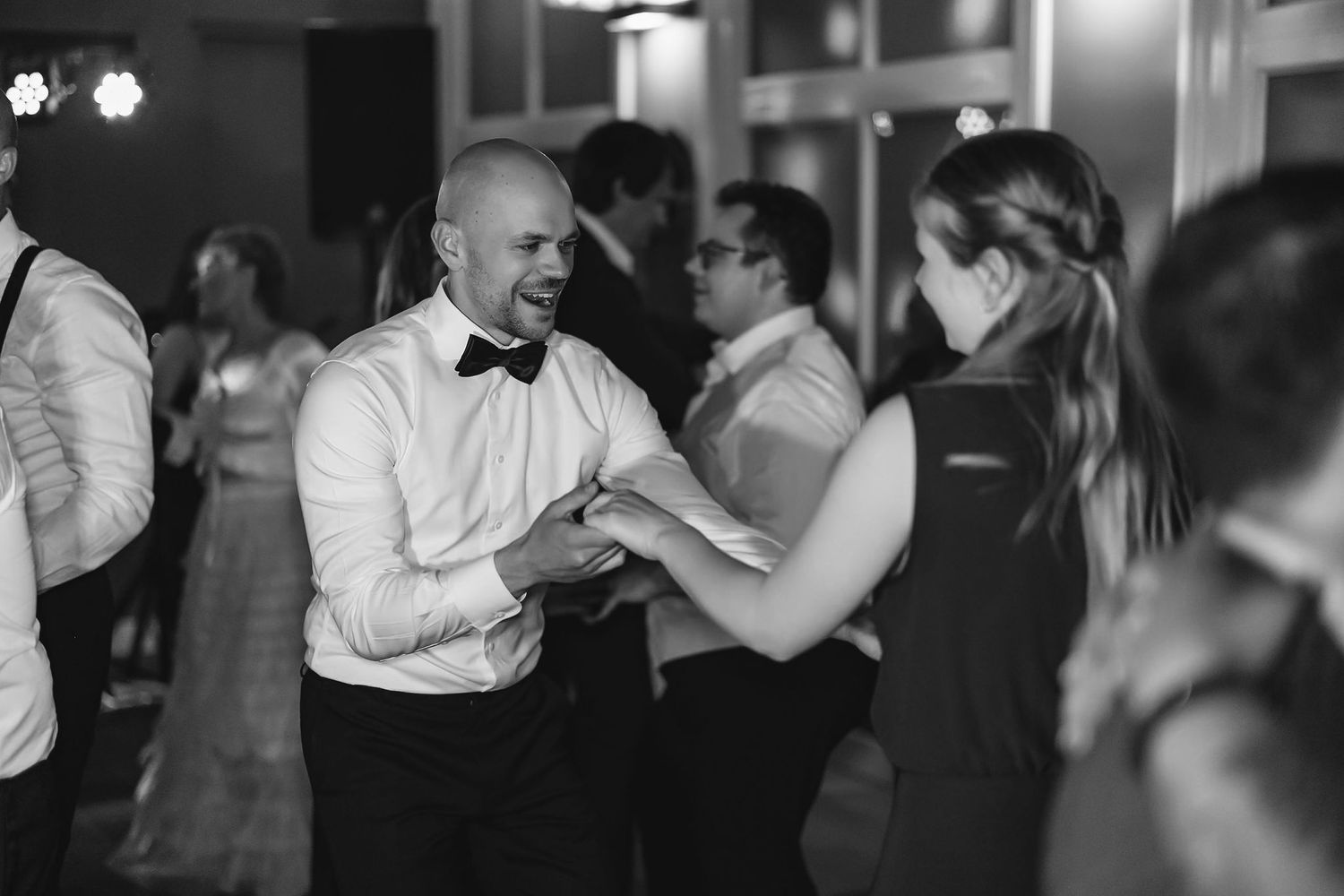 Wedding guests dancing together in dark reception venue with warm lighting.