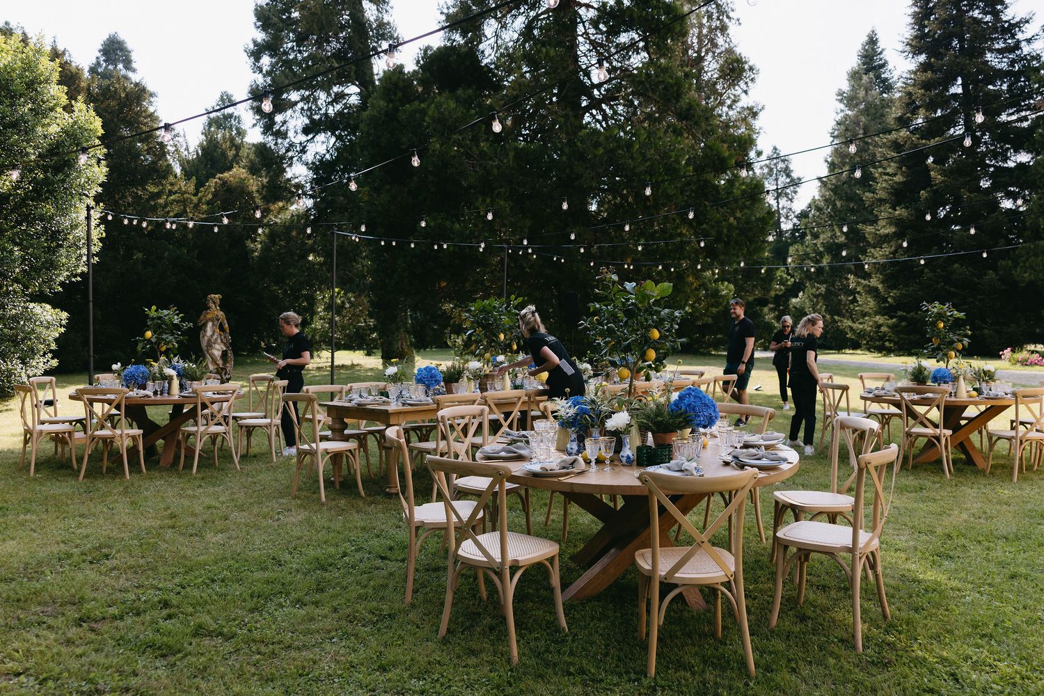 Rustic outdoor wedding reception setup with wooden chairs and tables in a garden setting.