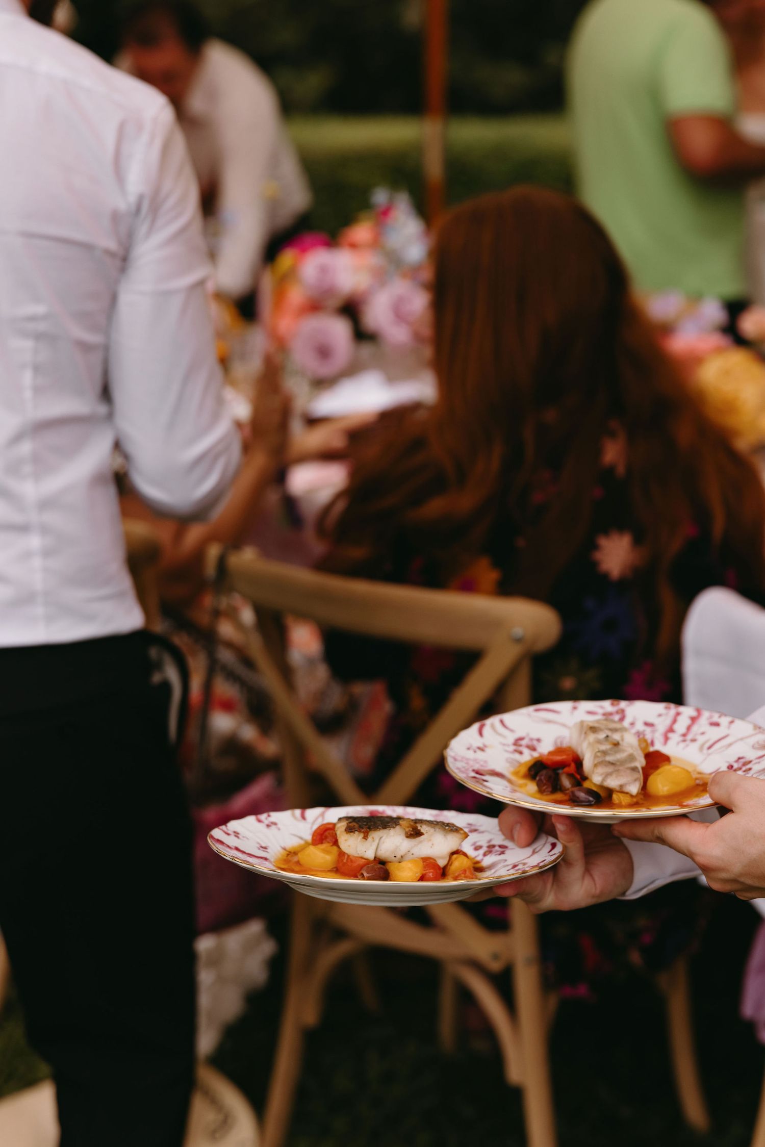 Catering staff serving food on decorative plates at an outdoor event.