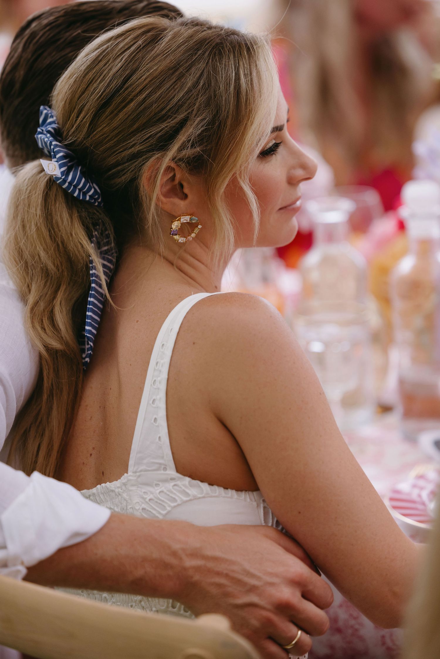 A wedding guest in a white sleeveless dress styled with an elegant updo and ribbon hair accessory.