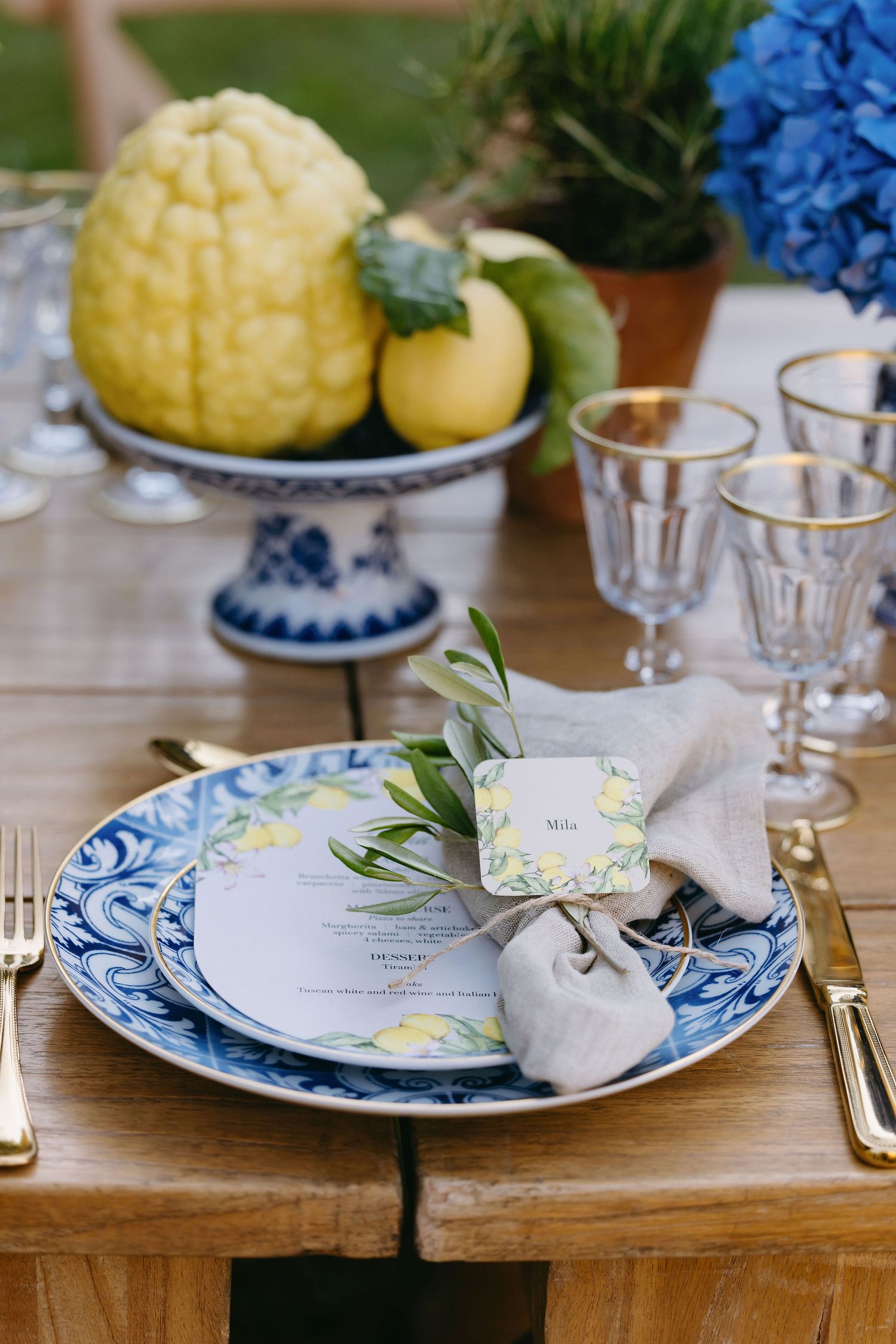 Elegant place setting with blue and white china plate, linen napkin, and citrus fruits on a wooden table.