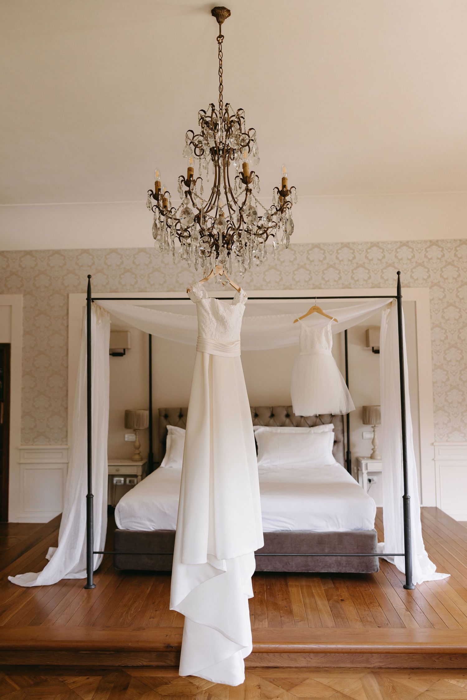 Wedding gown displayed on a hanger under an elegant crystal chandelier in a bridal suite.