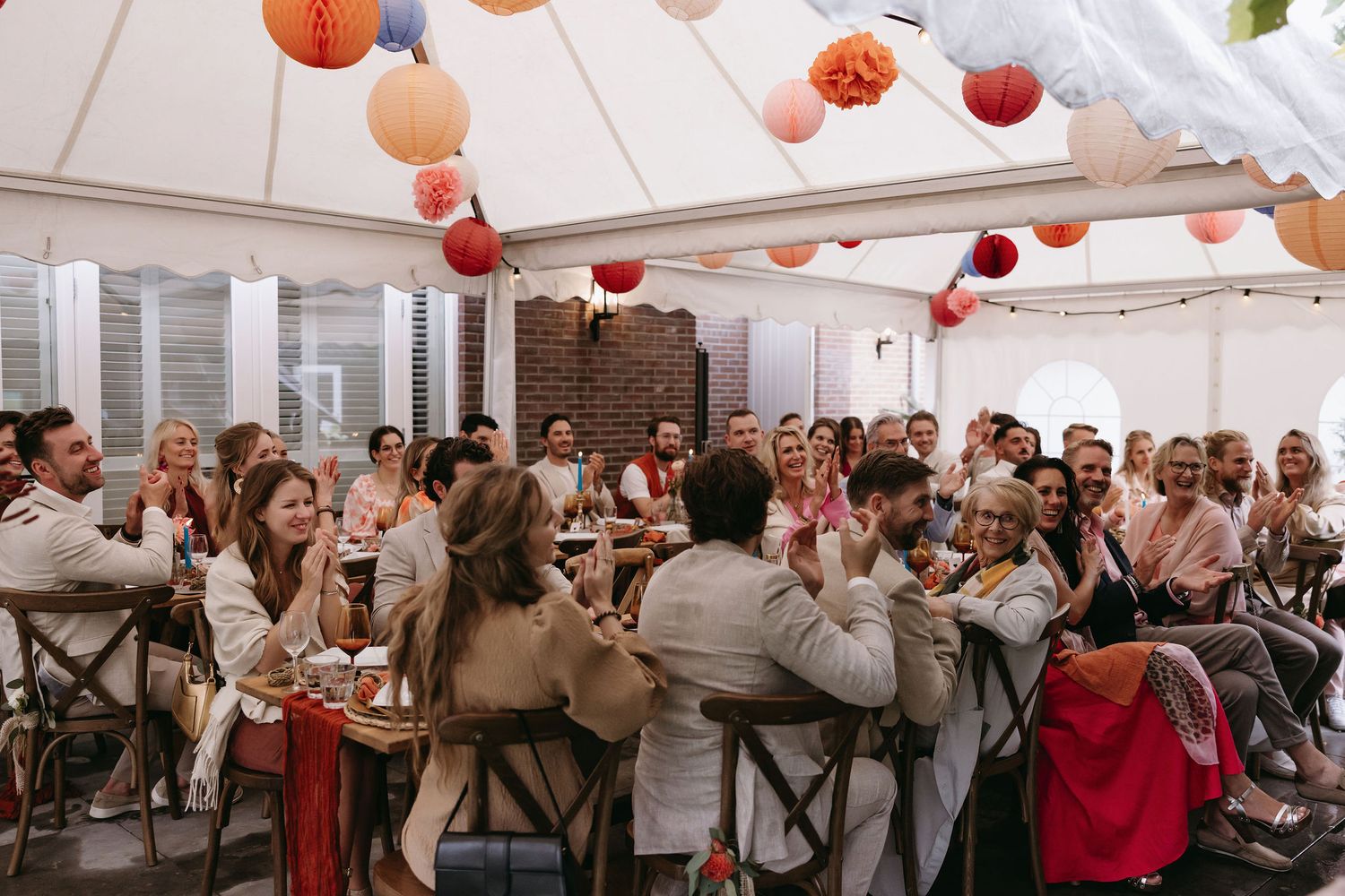 Wedding reception venue decorated with colorful paper lanterns as guests dine at long tables.