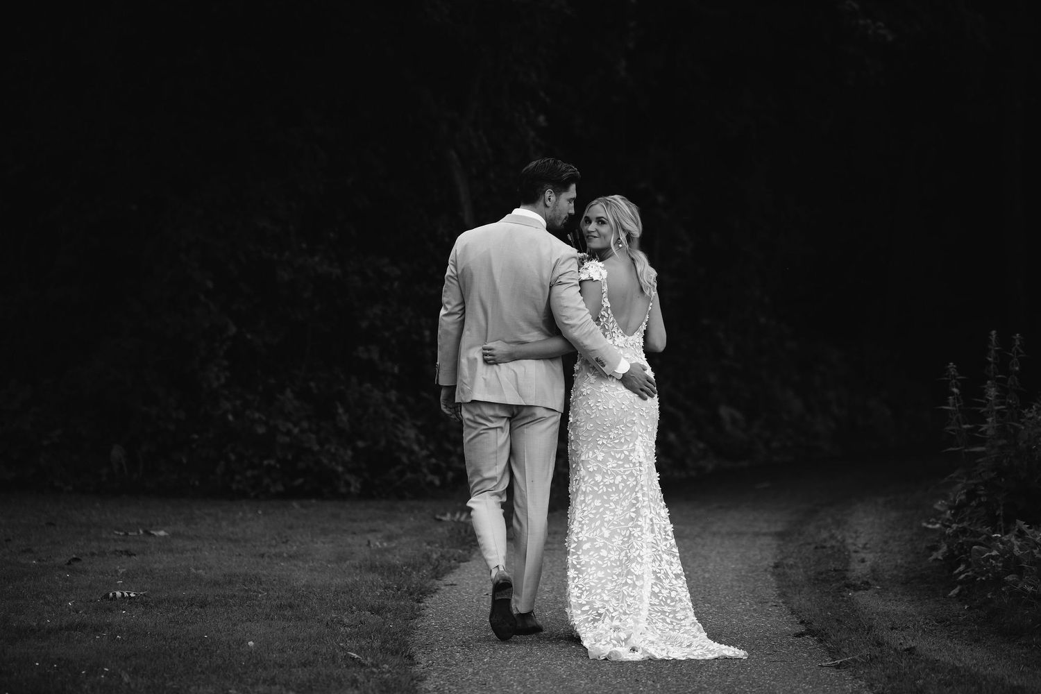 Black and white photo of newlyweds walking along garden path.