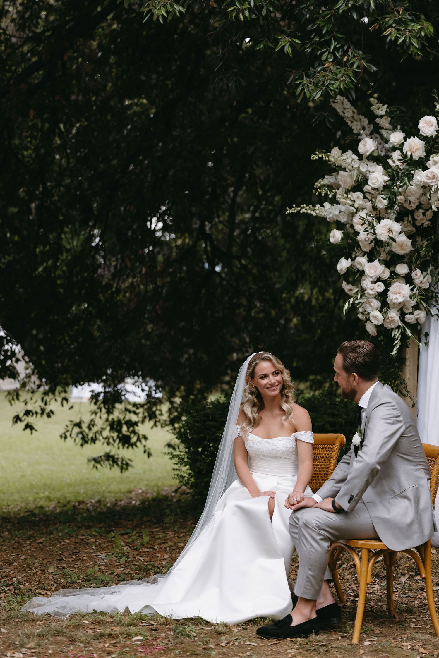A wedding couple seated under a tree with white floral decorations.