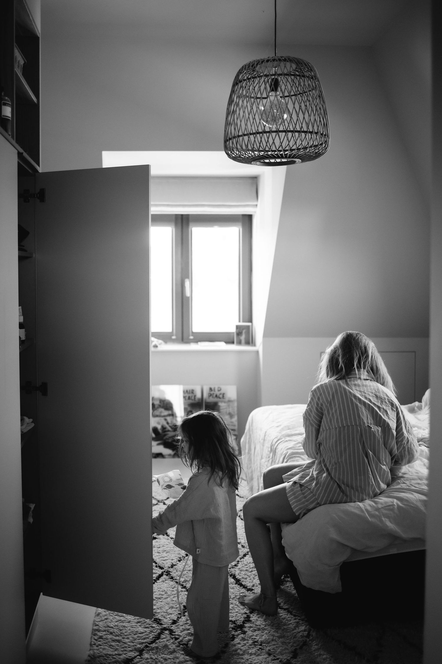 Black and white image showing silhouettes in bedroom with woven pendant light fixture.
