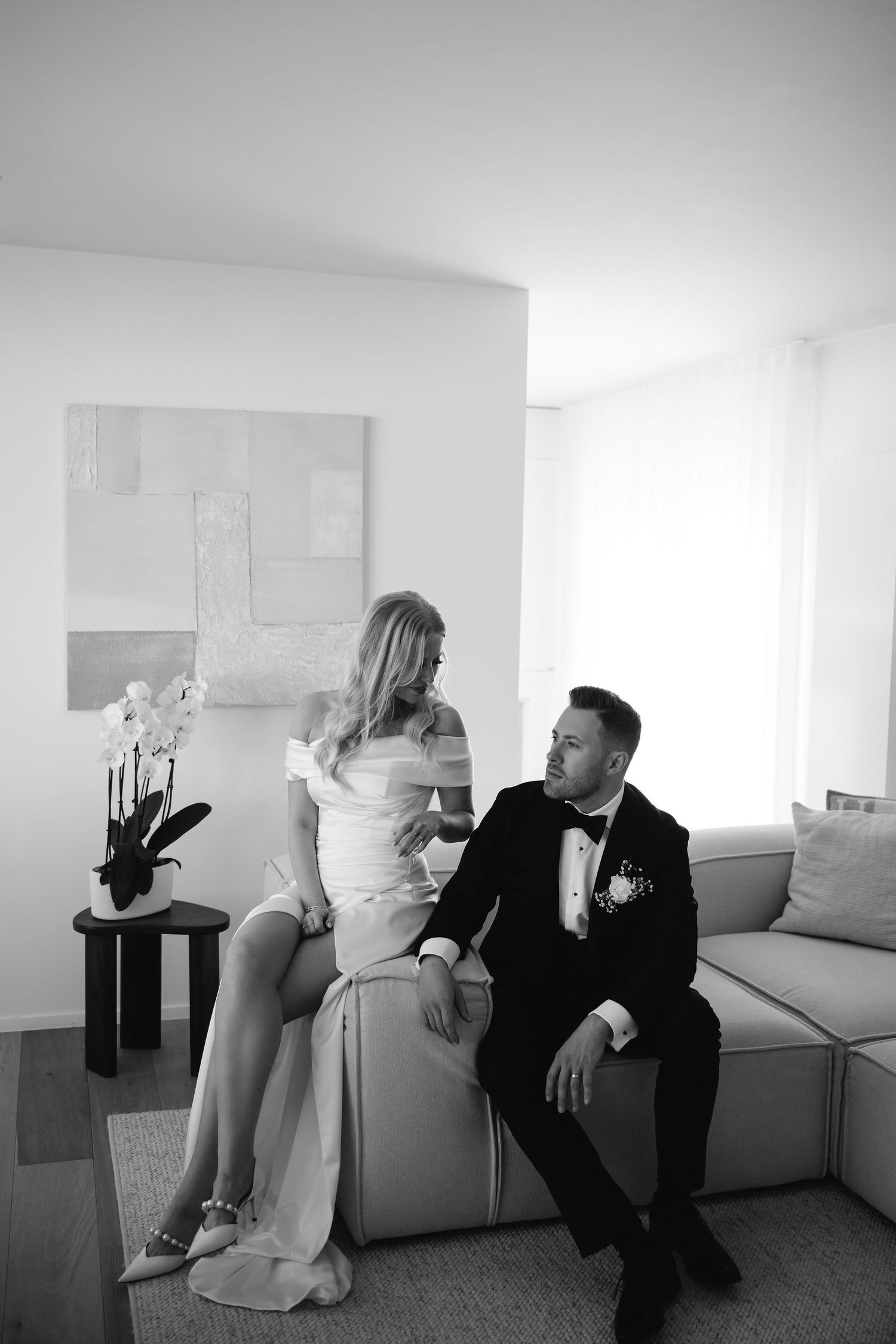 Black and white photo of newlyweds sharing an intimate moment on a modern sofa.