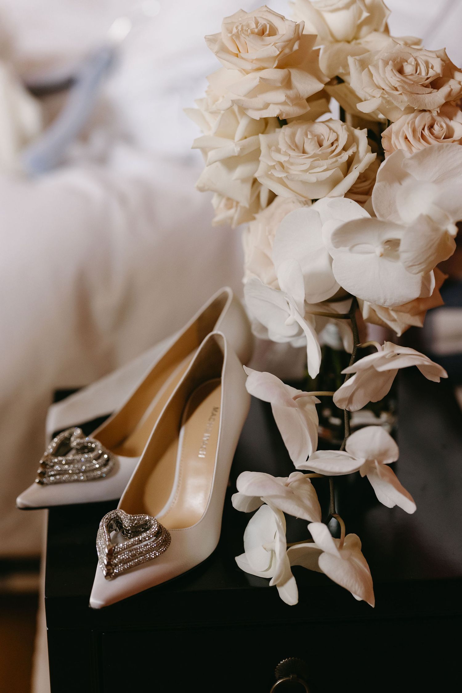Wedding day details featuring white roses and elegant bridal shoes with crystal embellishments.