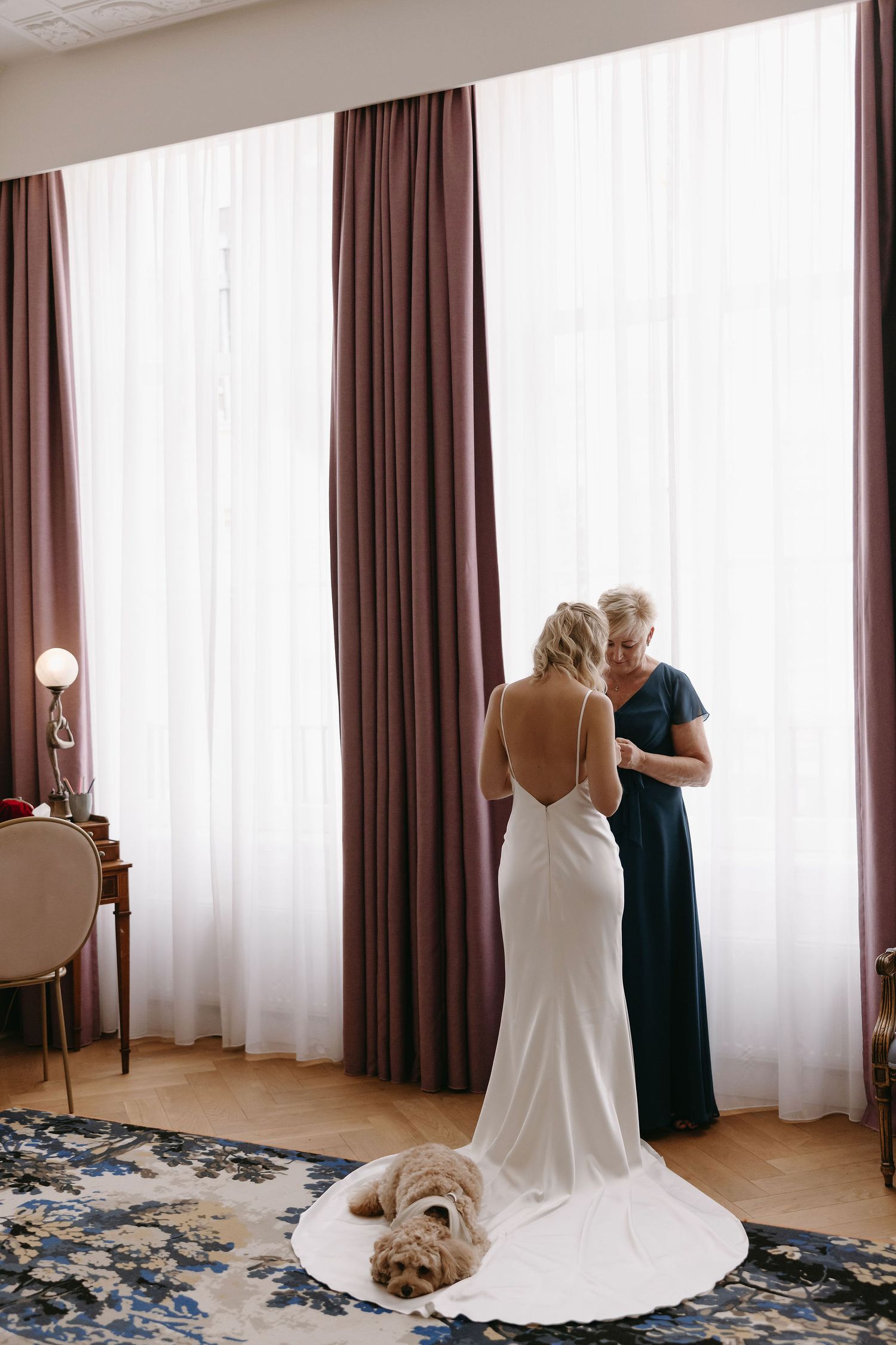 White backlit wedding dress with long train next to a sleeping dog in a modern hotel room.