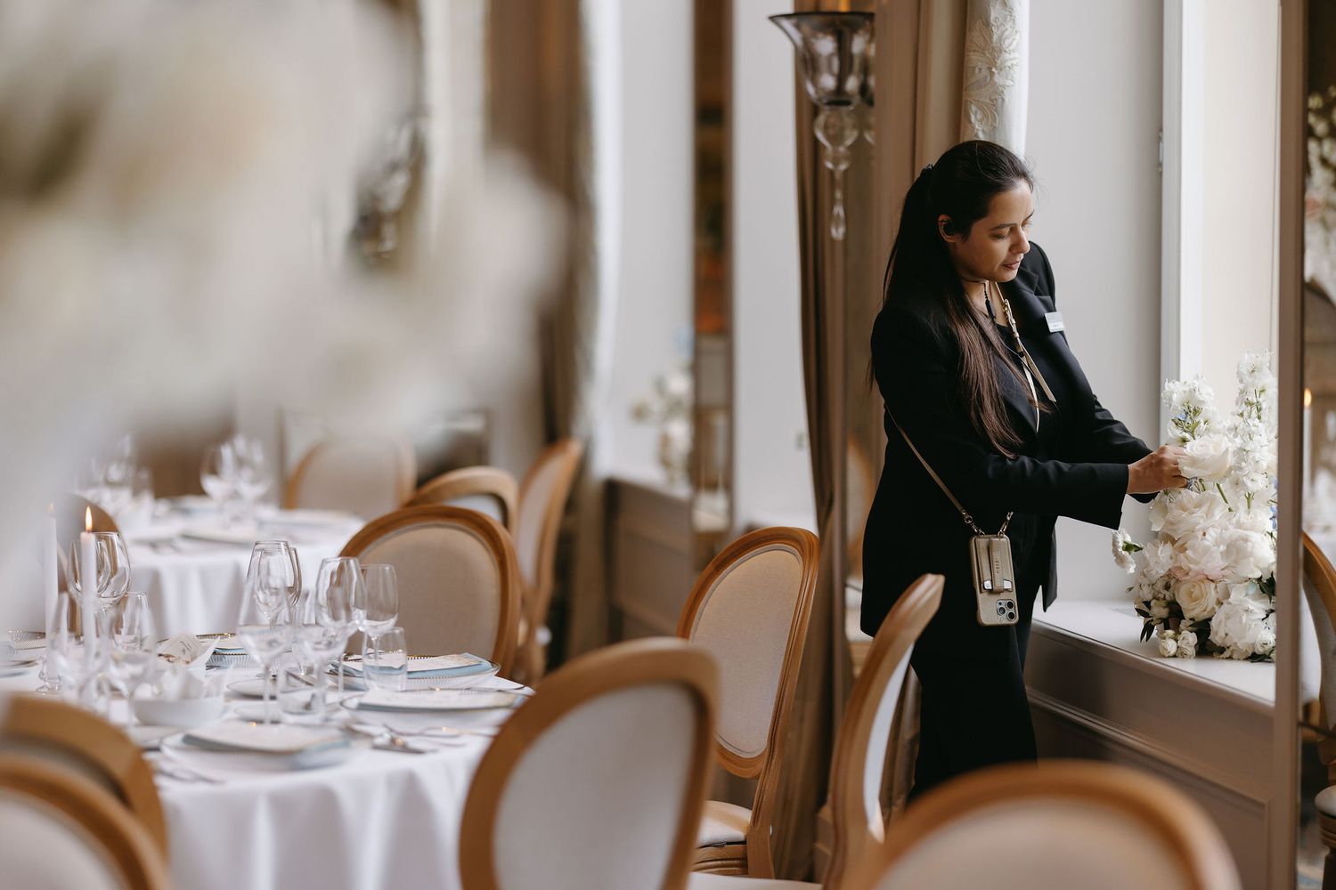 Event staff arranges table settings in an elegant dining room with white linens and classic decor.