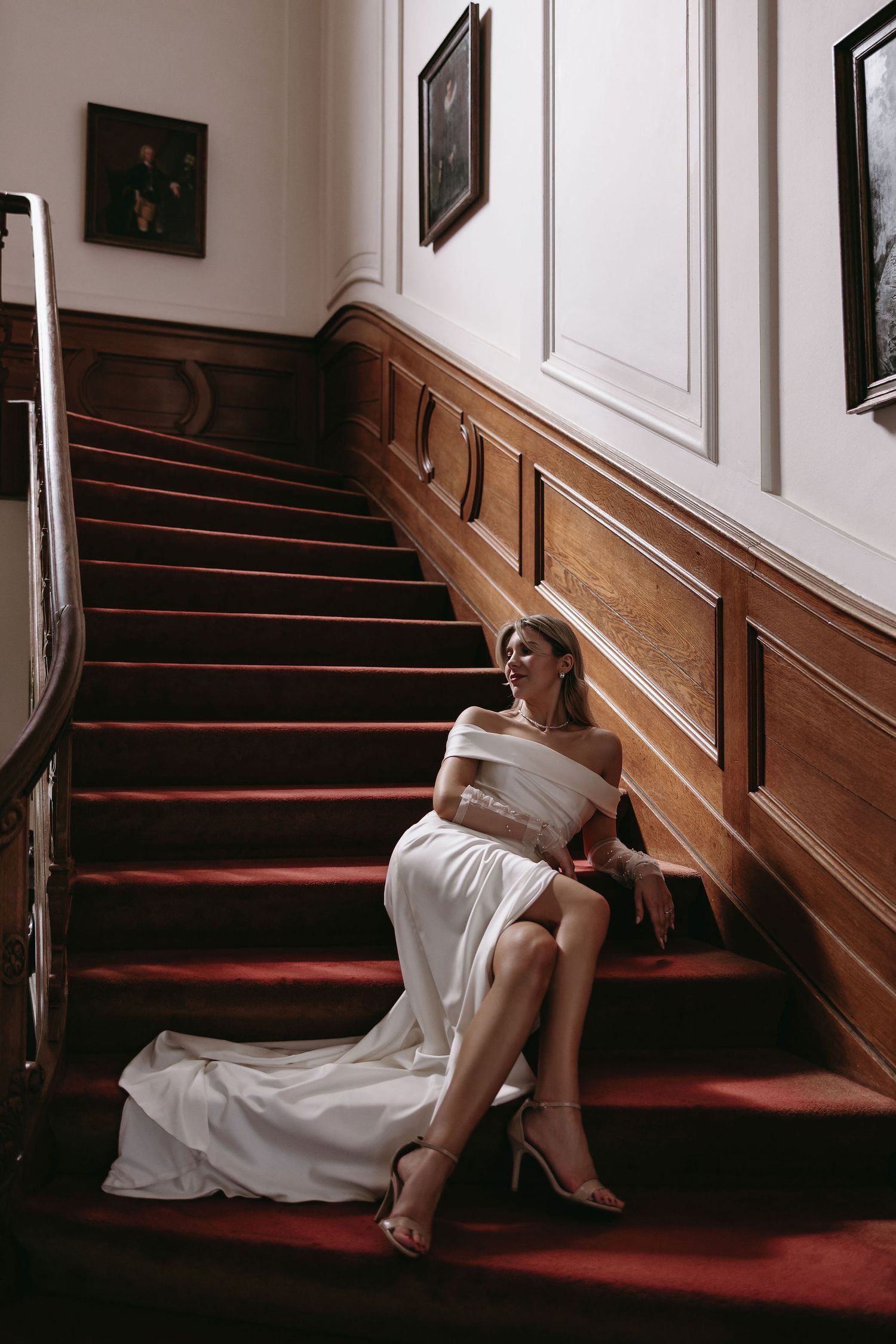 Elegant bridal photo on red carpeted stairs with wooden wainscoting and white walls in classic interior setting.
