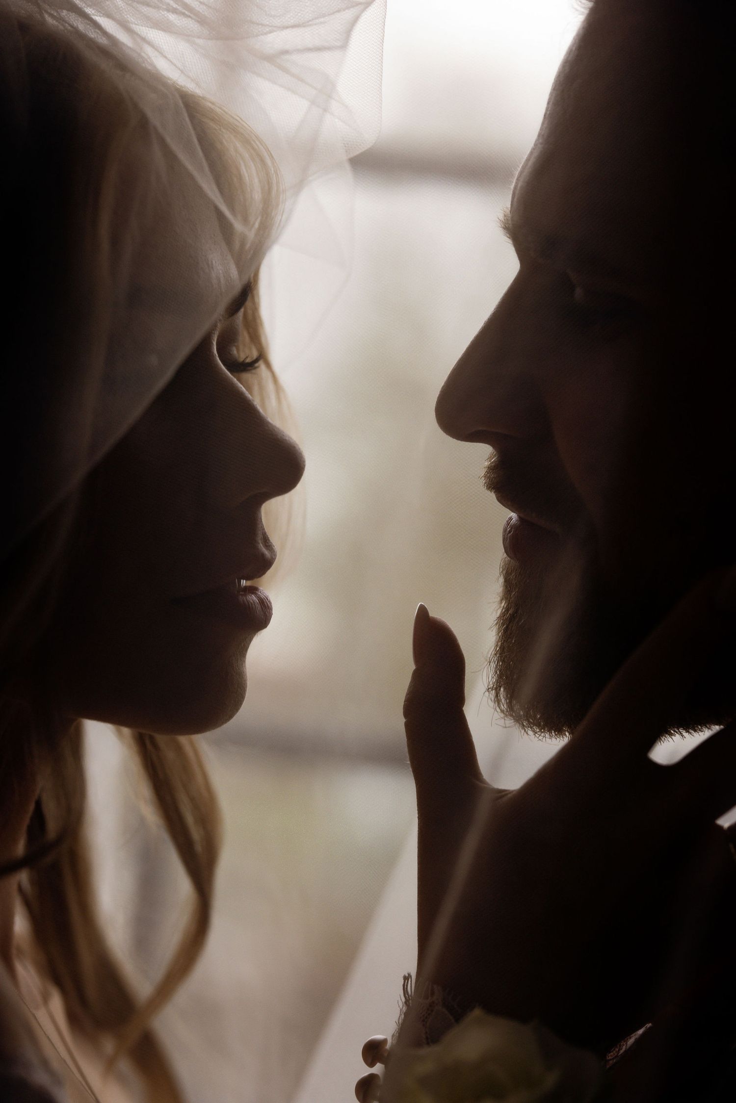 An intimate silhouette portrait of a couple in a tender romantic moment against soft window light.