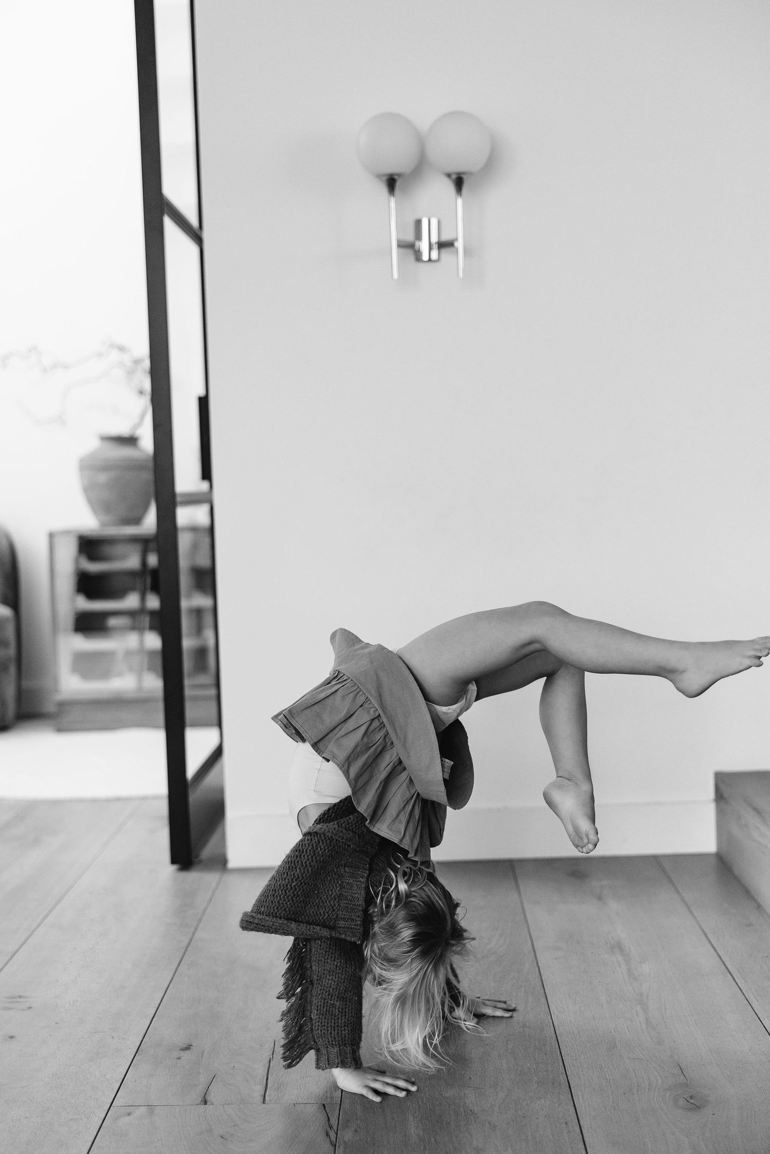 A playful black and white photo of someone doing a handstand in a flowing dress on a hardwood floor.