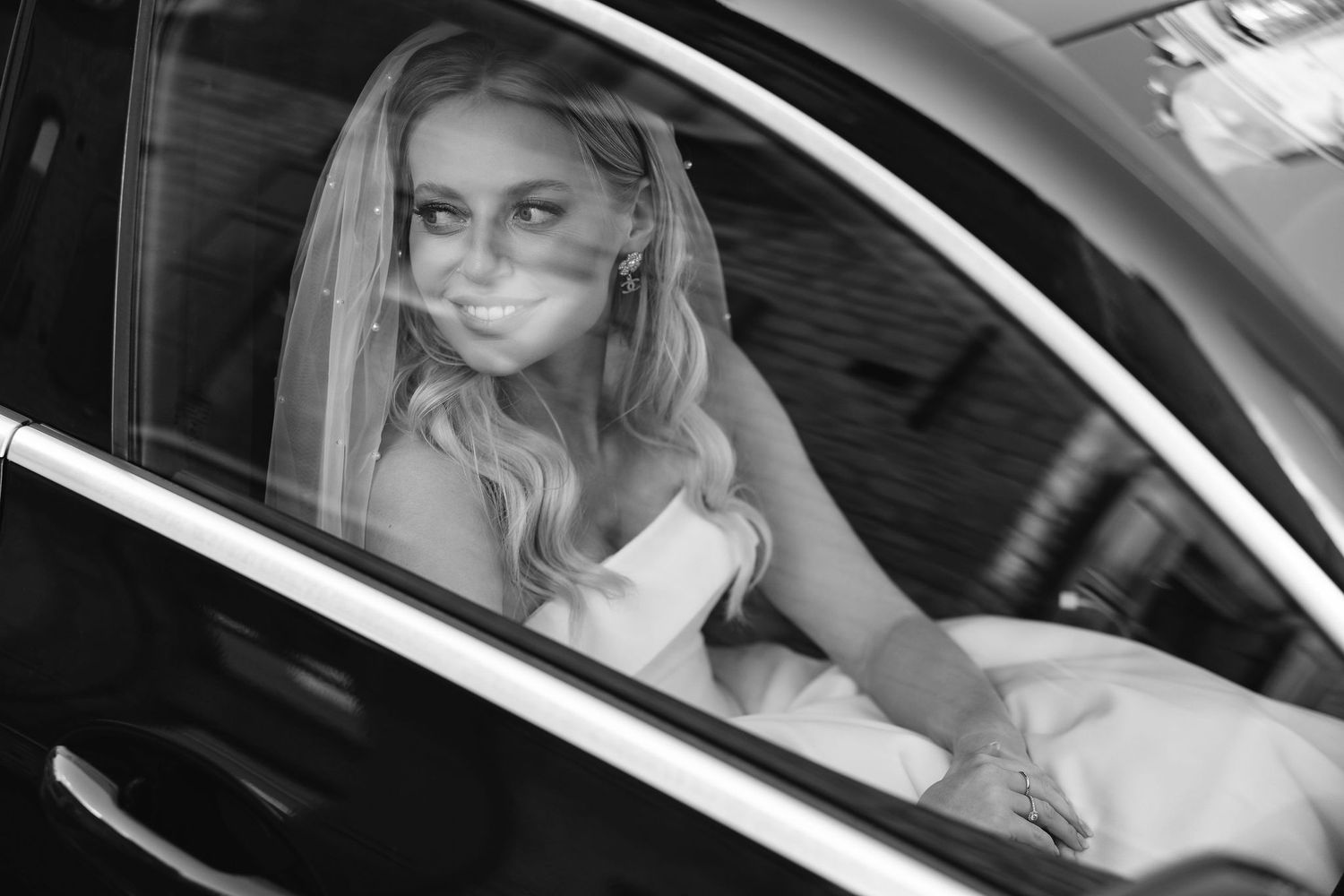 A black and white view through a car window showing someone in a white dress.