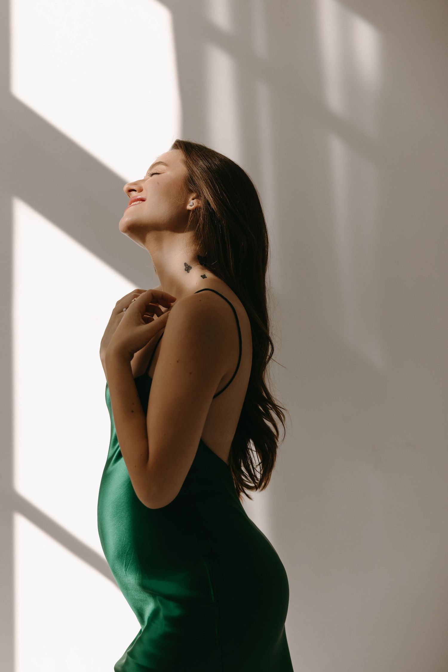 Woman in green top basking in dramatic window light against white wall.