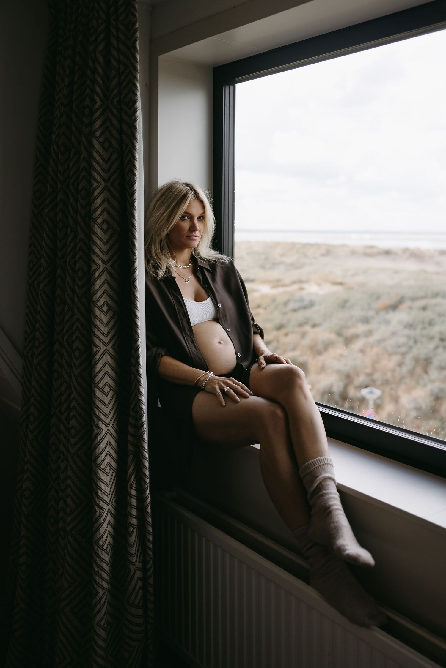 Intimate maternity photo by window overlooking natural landscape.