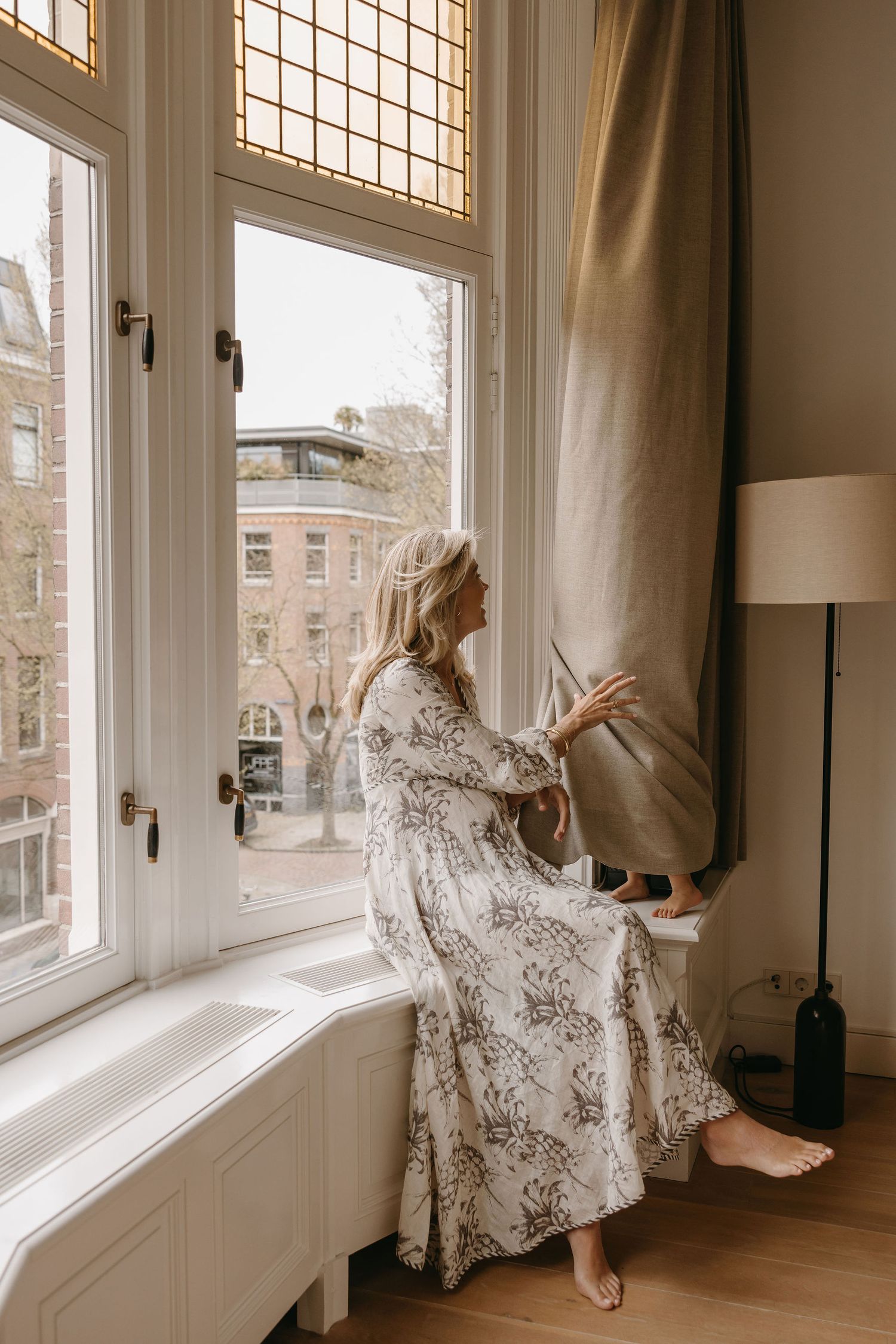 Artistic photos of someone in a patterned dress posing by large interior windows.
