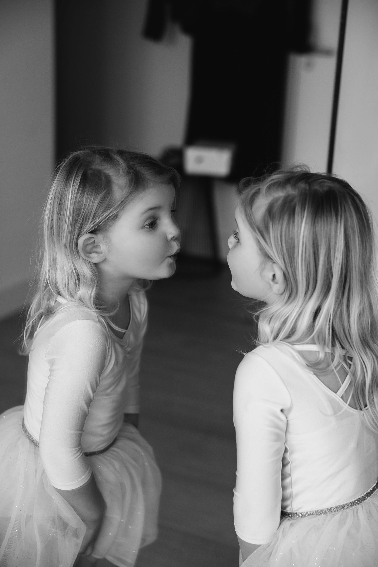 Two children in white outfits sharing secrets and giggles in a black and white photo.