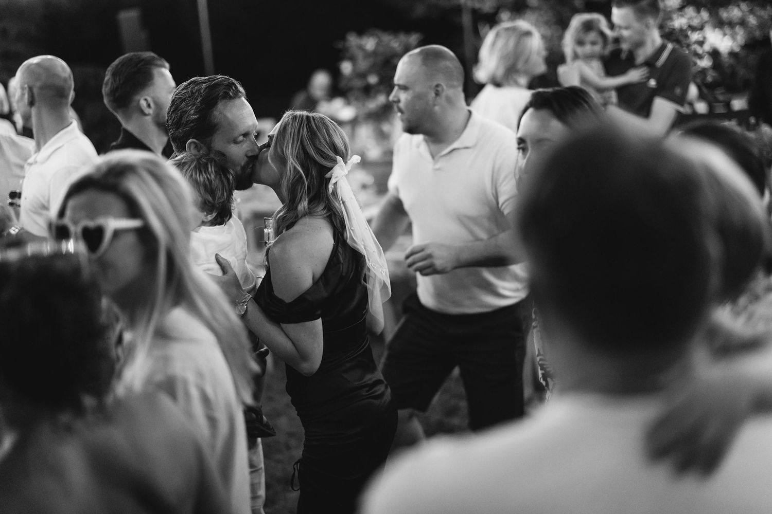 A crowded dance floor filled with wedding guests celebrating under outdoor lighting.