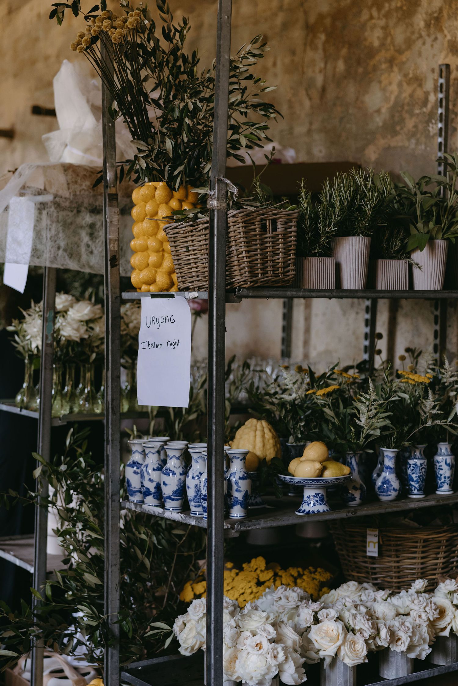 Floral styling station with yellow lemons, blue and white vases, and white flowers on industrial shelving.