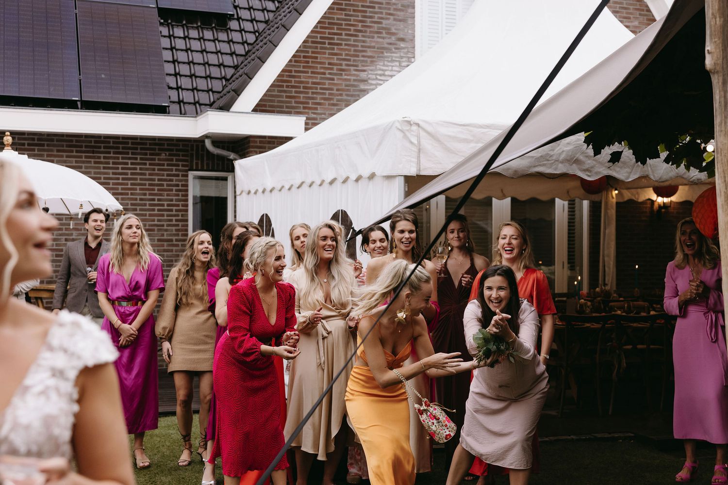 Wedding guests in colorful dresses gather under white reception tent.