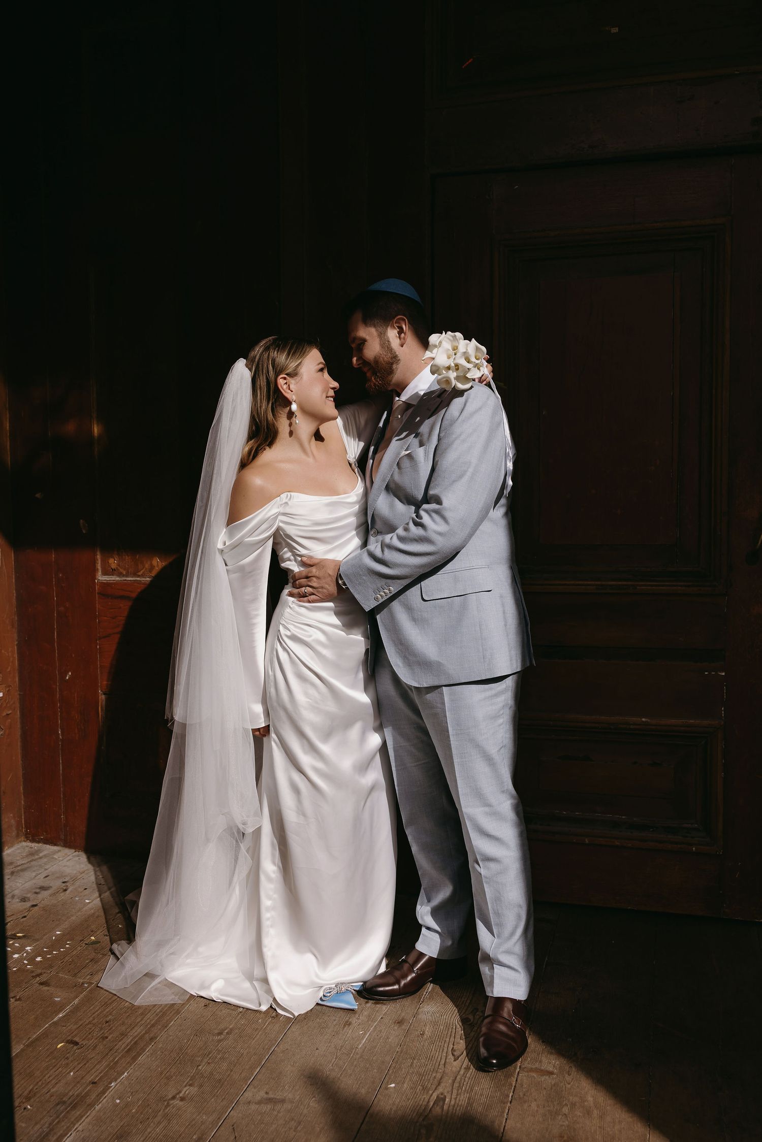 A couple sharing an intimate moment in formal attire against a dark wooden backdrop.