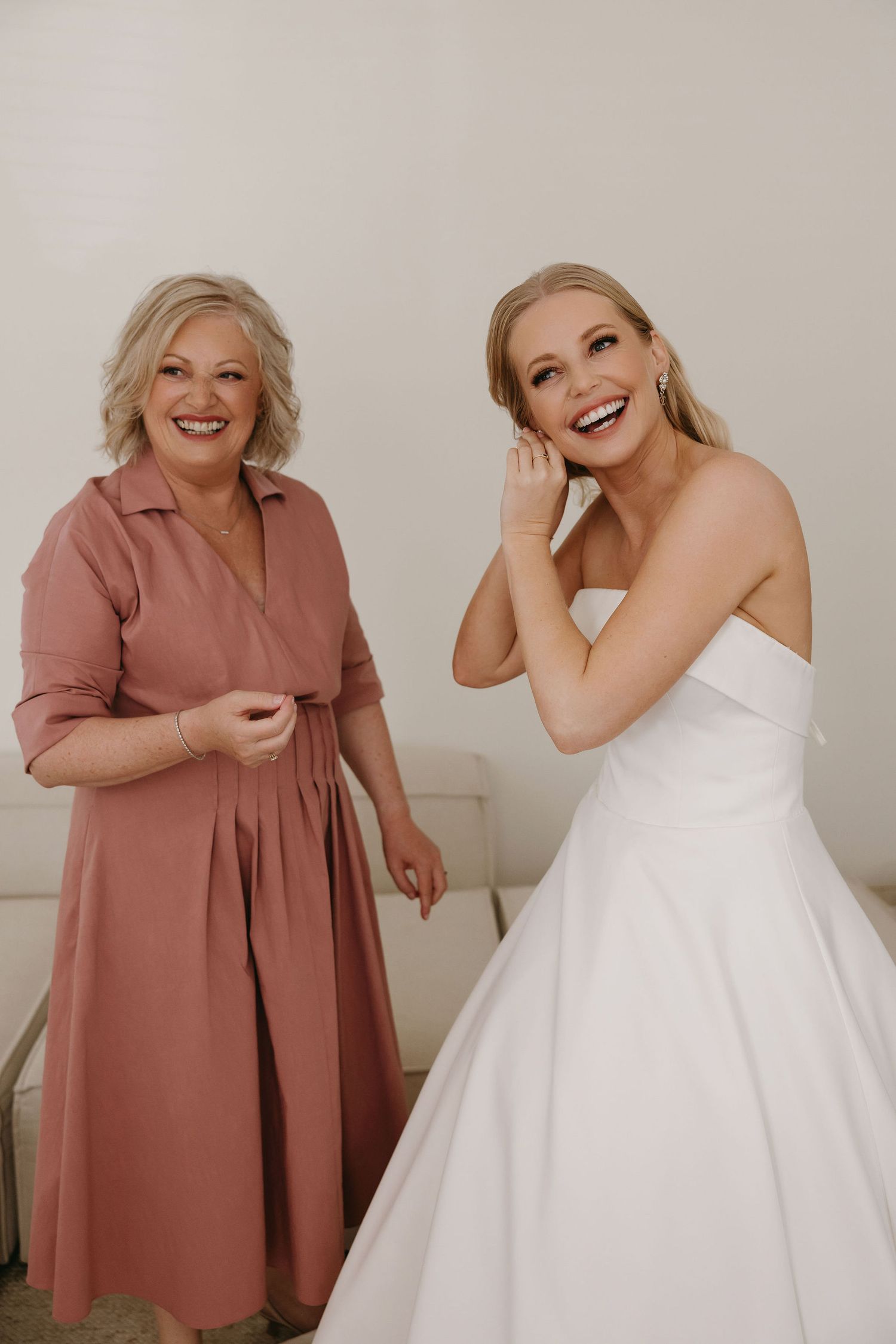 Two women share a joyful moment during wedding preparations in a bright room.