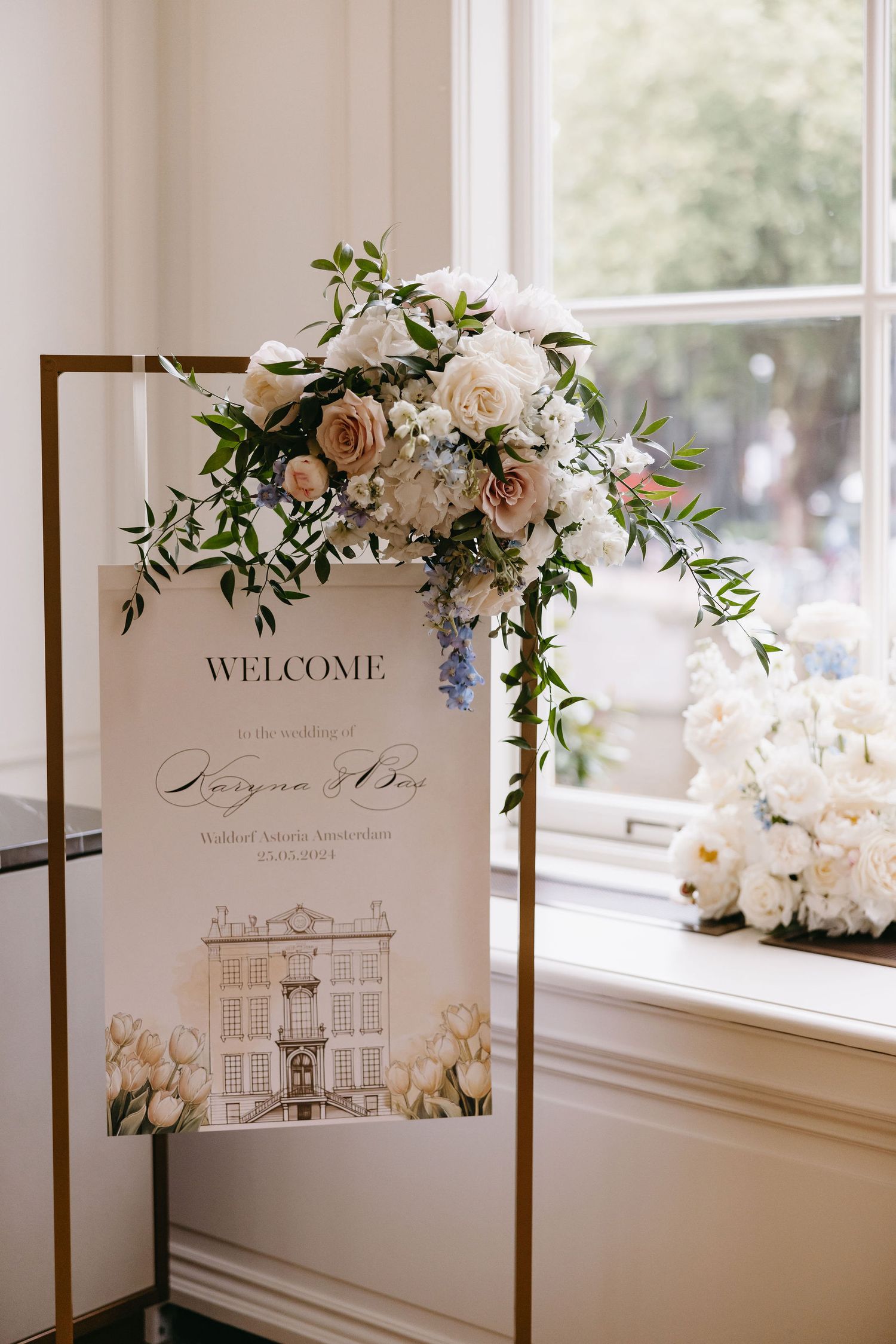 Elegant wedding welcome sign with floral arrangement featuring roses and greenery.